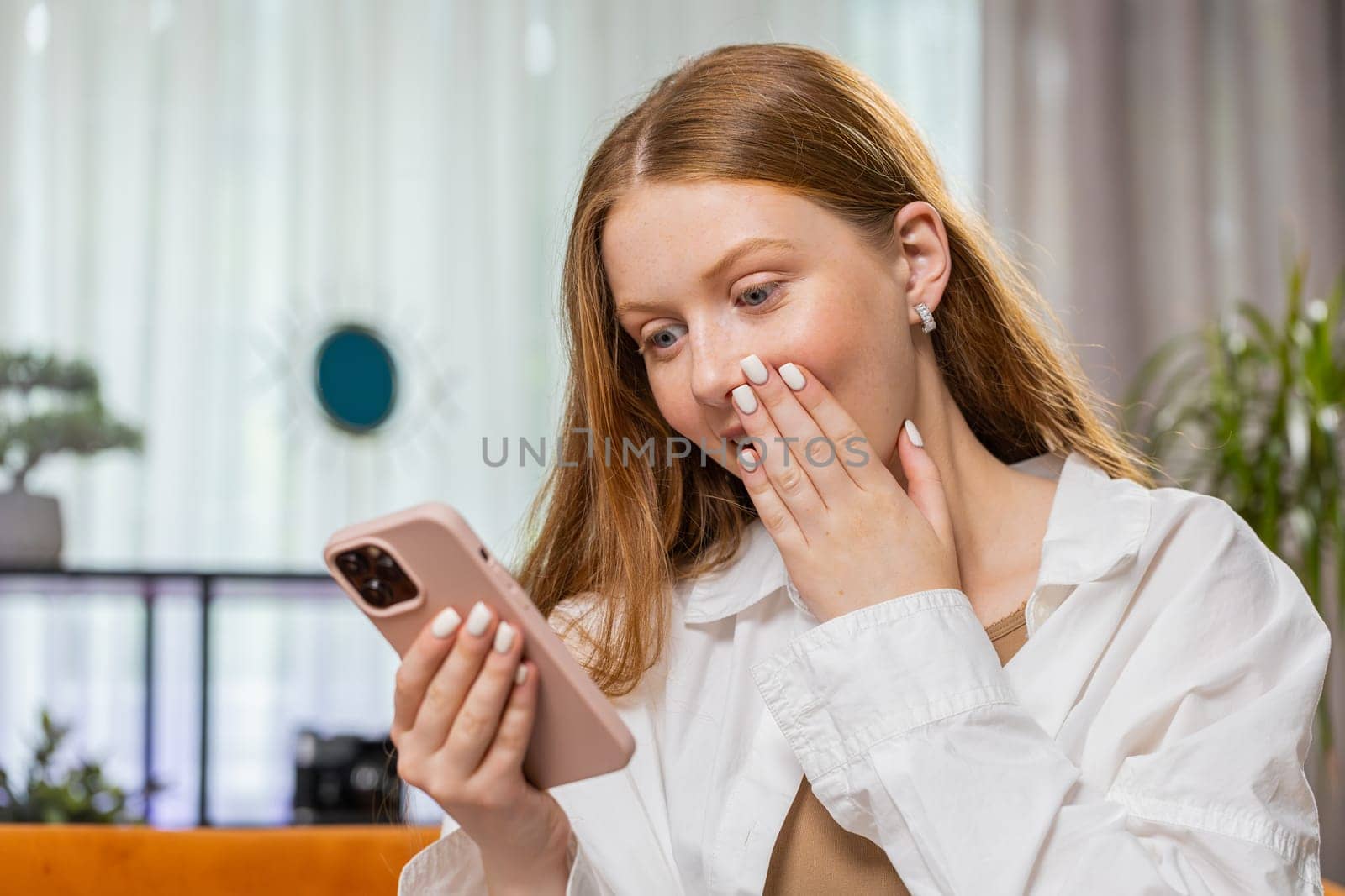 Happy teenager girl use mobile smartphone typing browsing say Wow yes found out great big win good news celebrate lottery jackpot, play victory game. Portrait of child at home in room sitting on sofa