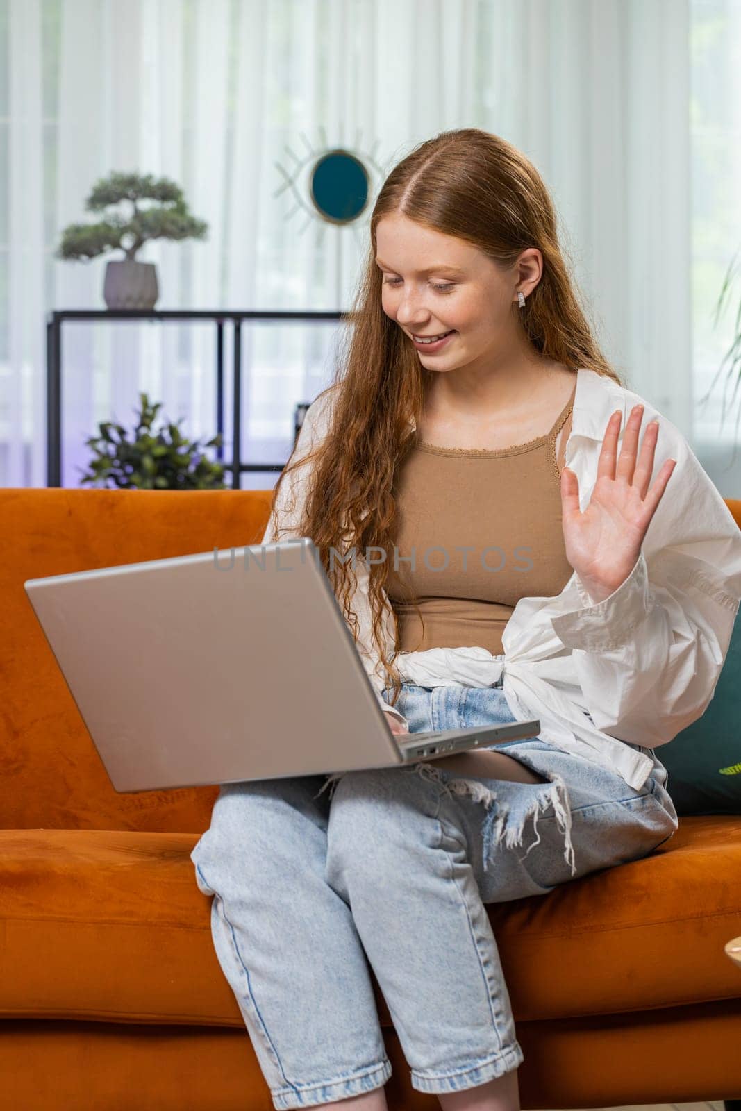 Teenager girl making video webcam conference call with friends or family, enjoying pleasant conversation. Child use laptop to talk with teacher, study, education at home sitting on room sofa. Vertical