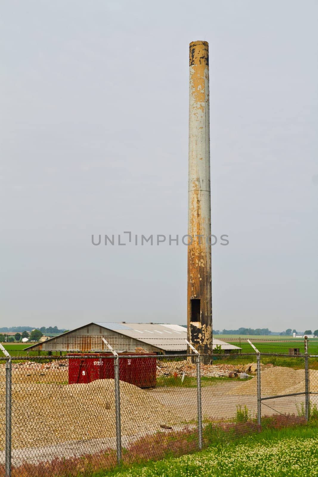 Capturing the faded grandeur of an abandoned industrial site in Evansville, Indiana. A towering smokestack looms over a neglected warehouse in the tranquil rural setting, evoking themes of industrial decline and the passage of time.