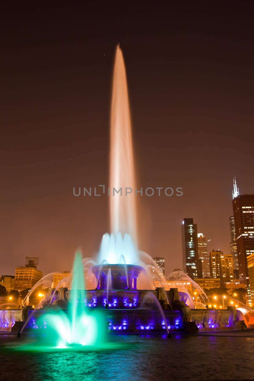 Colorful Cityscape: Vibrant illuminated fountain stands tall amidst Chicagos urban skyline at night, creating a captivating display of water jets and dancing lights.