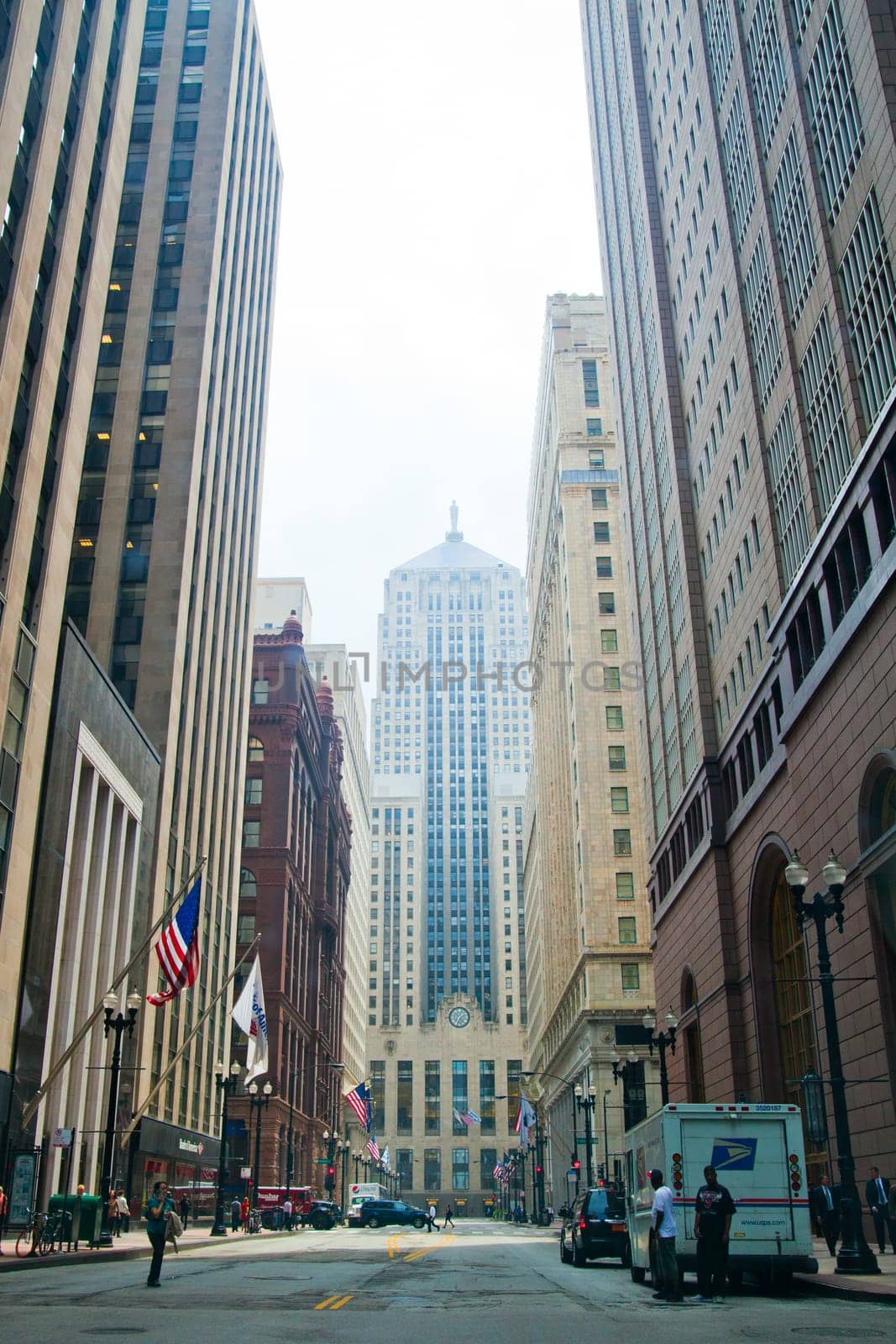Dynamic Cityscape of Chicago's Downtown: A blend of historic and modern architecture defines the skyline, as a quiet urban street comes alive with daily life activity and American flags waving proudly.