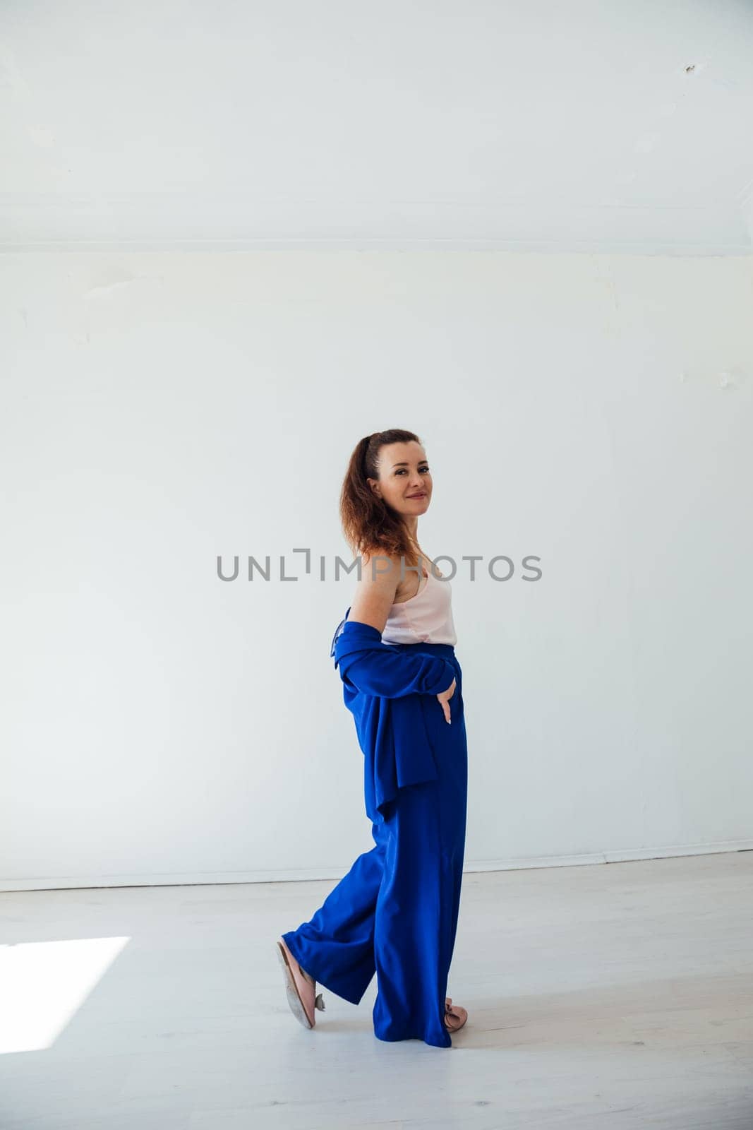 Beautiful brunette woman in blue summer suit posing in white room