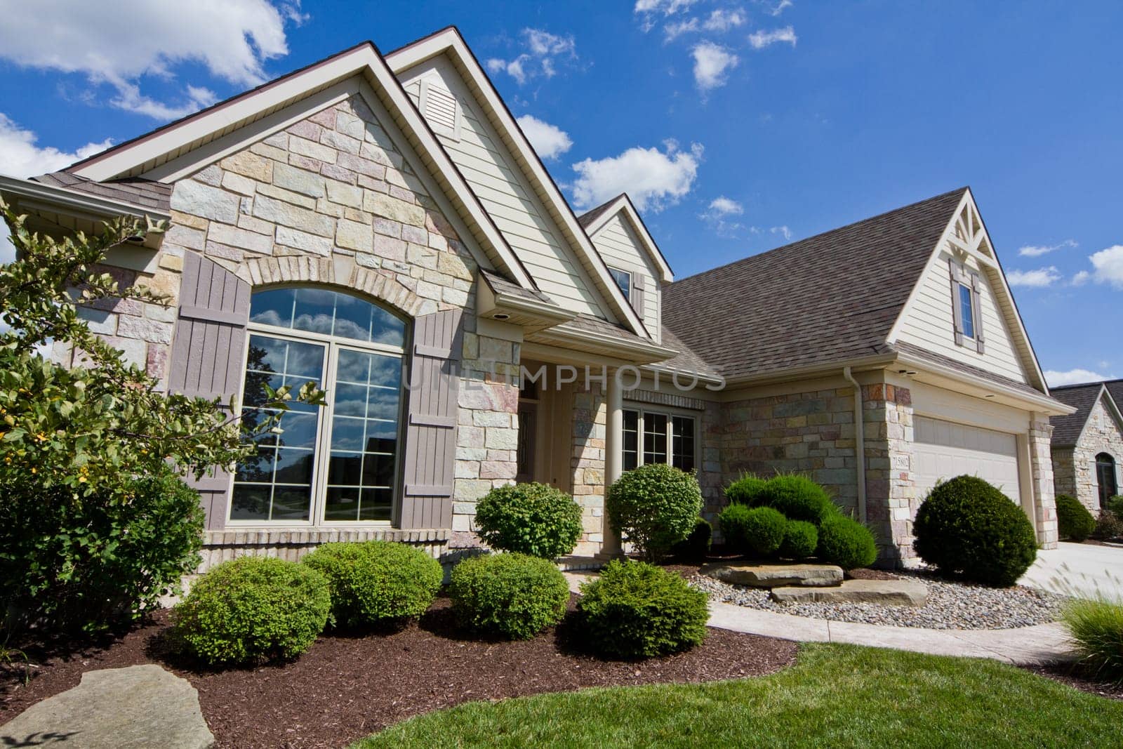 Modern suburban dream home in Fort Wayne, Indiana. This spacious single-family residence features a stunning combination of stone and siding, with an arched window and a gable roof. A well-maintained front yard.
