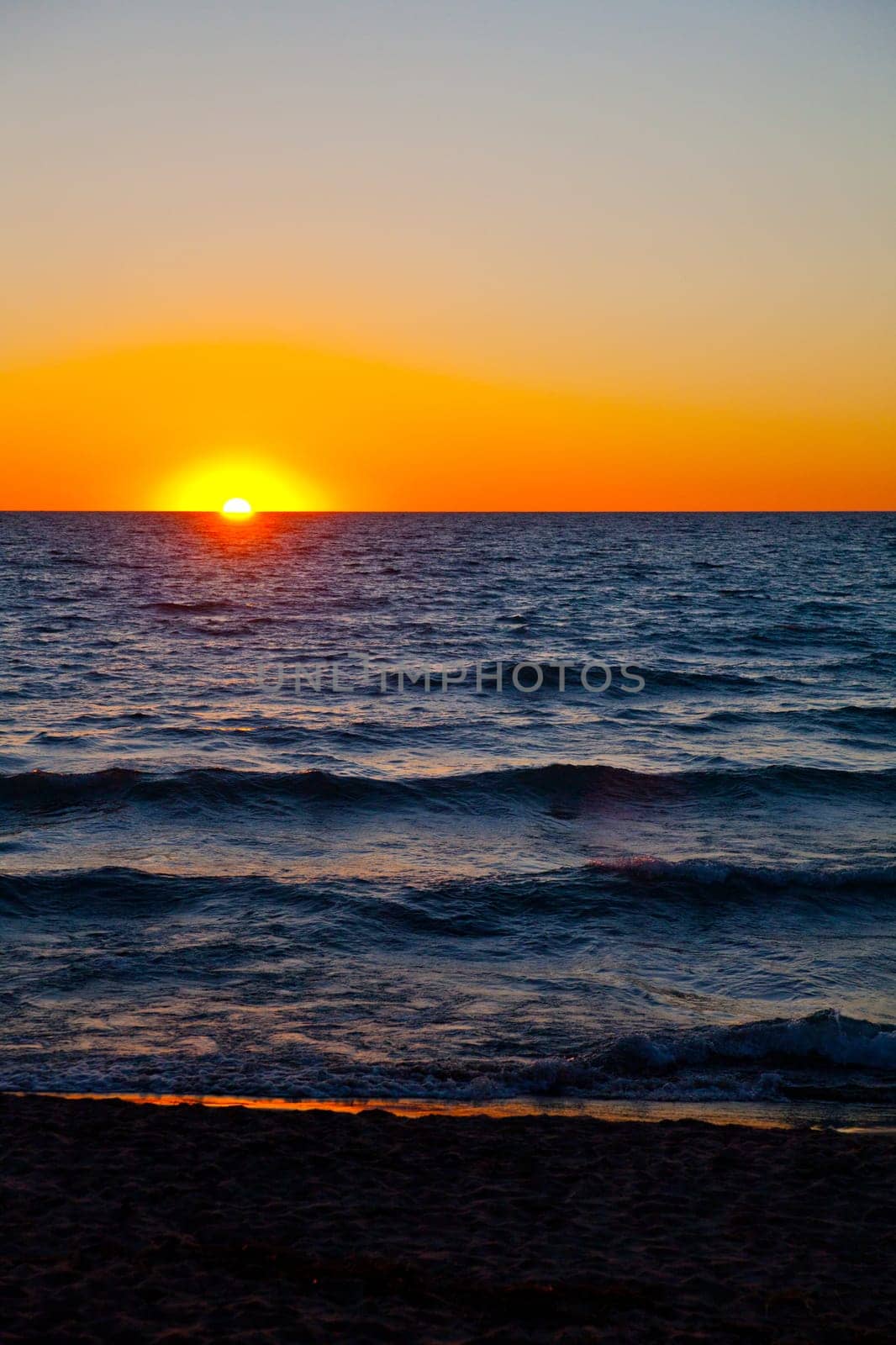 Mesmerizing sunset over Lake Michigan, casting a vibrant orange glow on the expansive beach. Tranquil and serene, a perfect natural landscape.