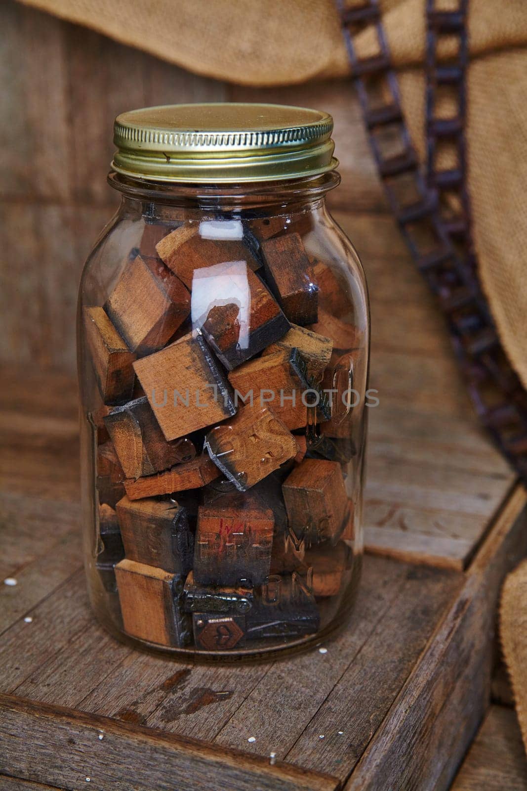 Vintage wooden letterpress blocks in a glass jar on a worn wooden surface, evoking nostalgia and artistic charm. Perfect for graphic designers, vintage decor enthusiasts, and artisanal crafters.