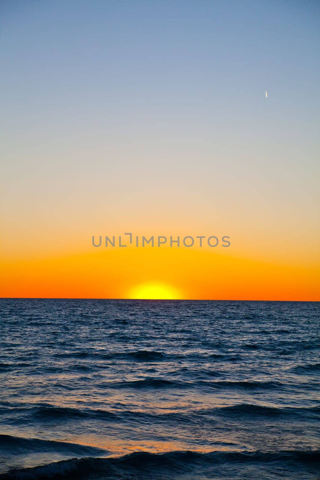 Tranquil sunset over the ocean, with vibrant hues of orange and yellow painting the sky. The calm waves reflect the golden hour glow, creating a serene atmosphere. Ideal for conveying peace, closure, and natural beauty.