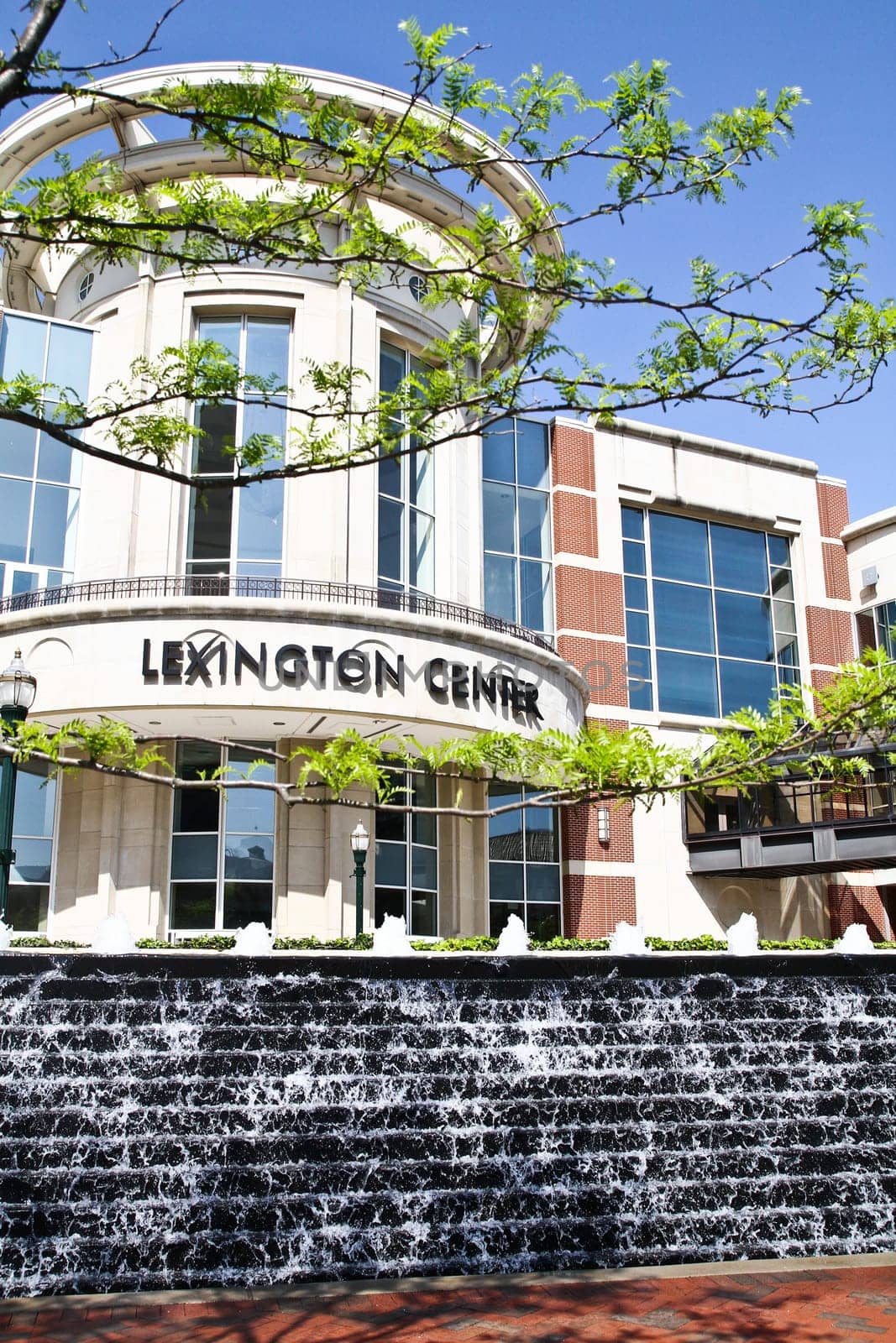 Lexington Center: A stunning modern architectural marvel with a curved glass feature and vibrant cream and brick red facade. The center's name shines on a metallic sign, while a captivating water feature adds a touch of natural serenety.