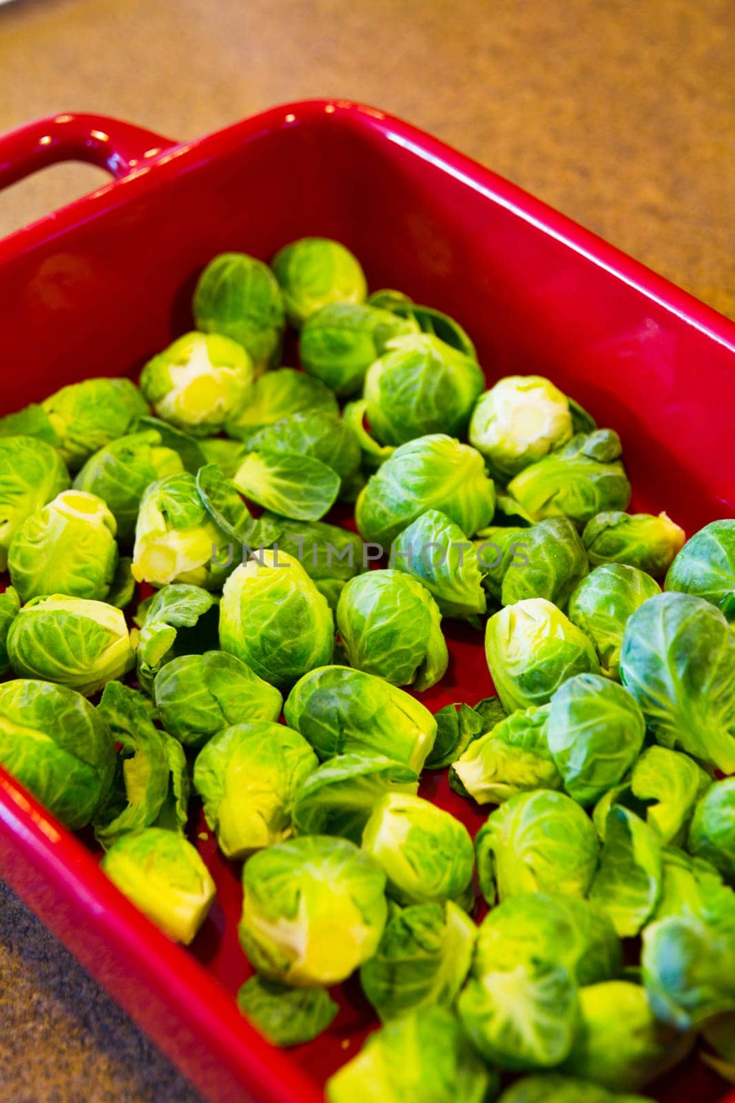 Fresh Brussels Sprouts in Red Baking Dish on Kitchen Countertop by njproductions