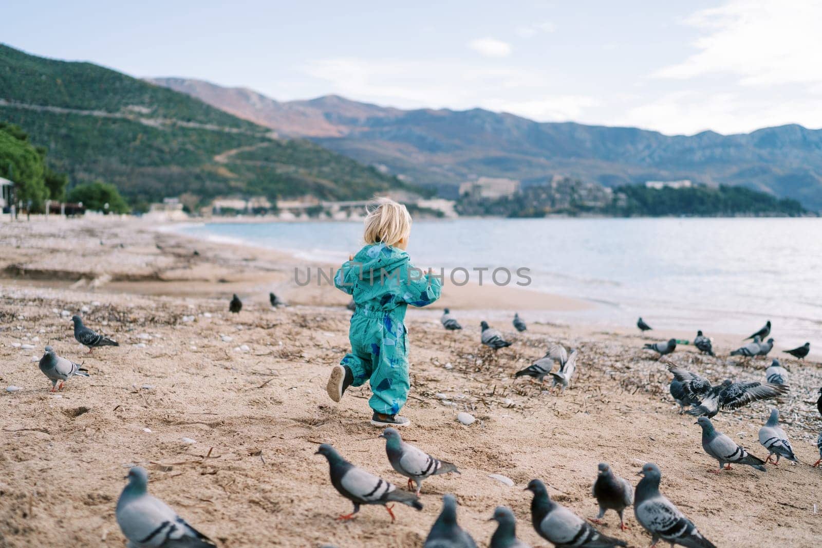 Little girl chasing pigeons along the seashore. High quality photo