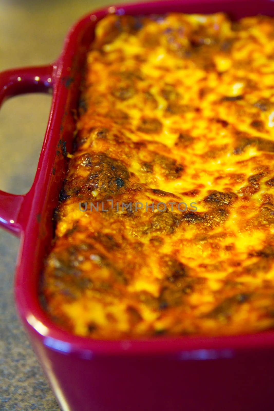 Indulge in a mouthwatering baked casserole masterpiece, featuring a golden-brown, bubbling cheese crust, served in a vibrant red dish. Perfect comfort food for family meals and culinary delights.