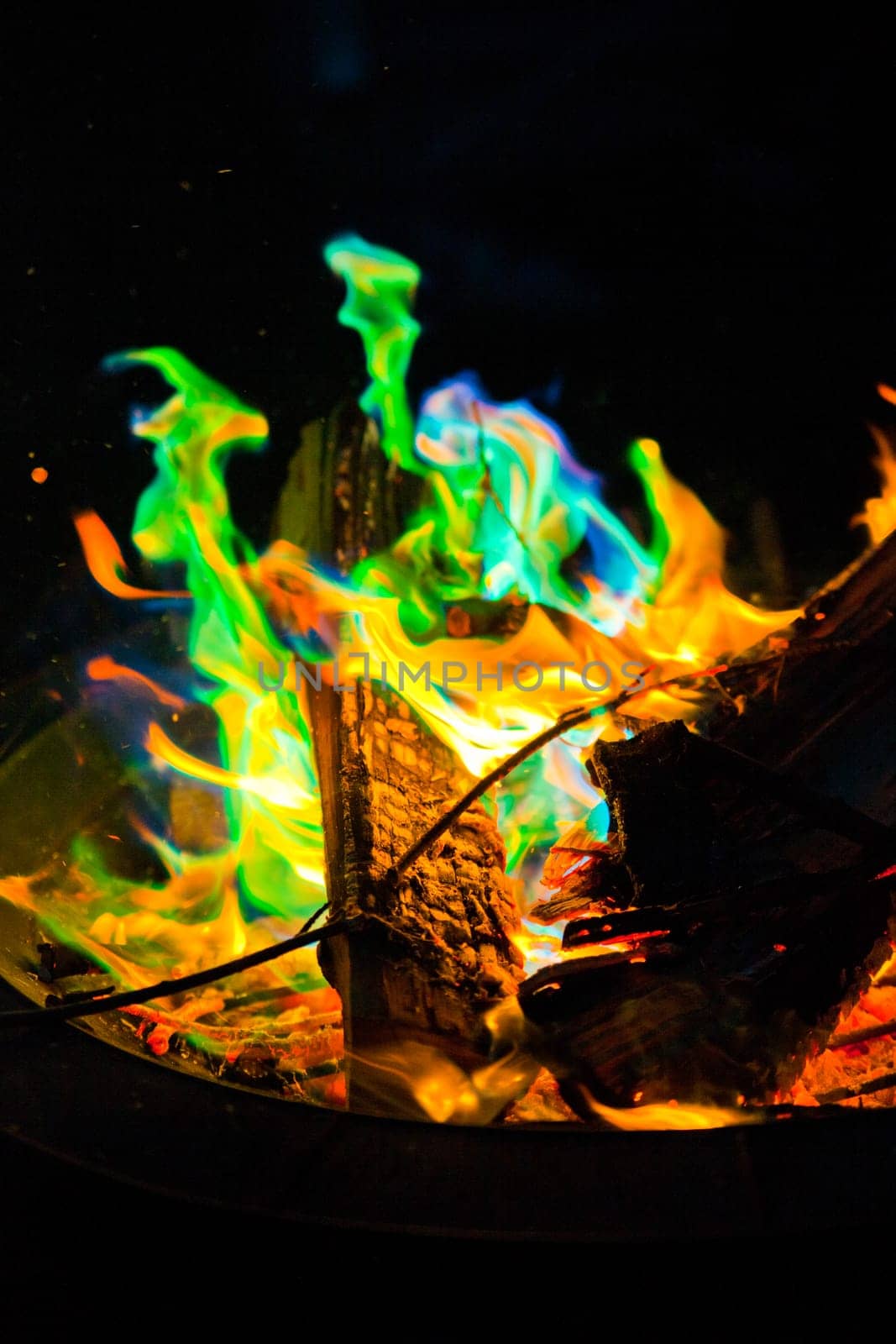 Experience the mesmerizing dance of vibrant flames in a captivating fire pit. The enchanting blend of green, blue, and traditional orange hues creates a magical display. Shot in a close-up perspective.