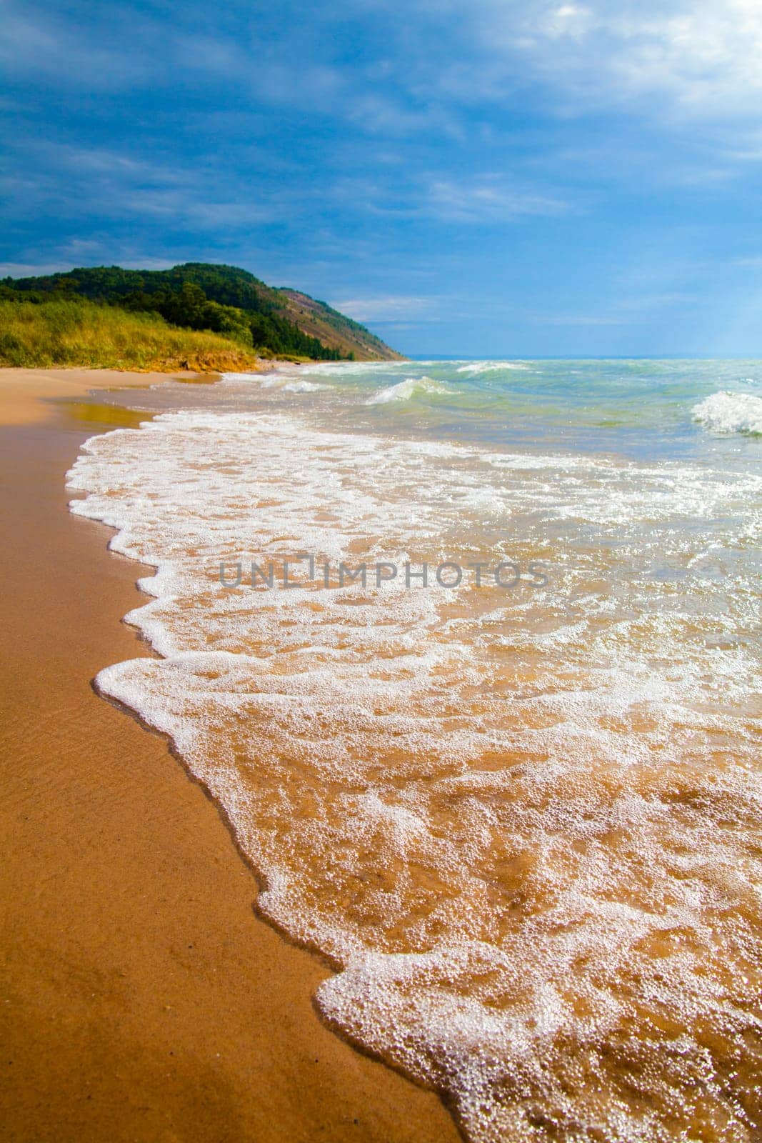 Tranquil Michigan Beach with Frothy Waves and Lush Hillside by njproductions