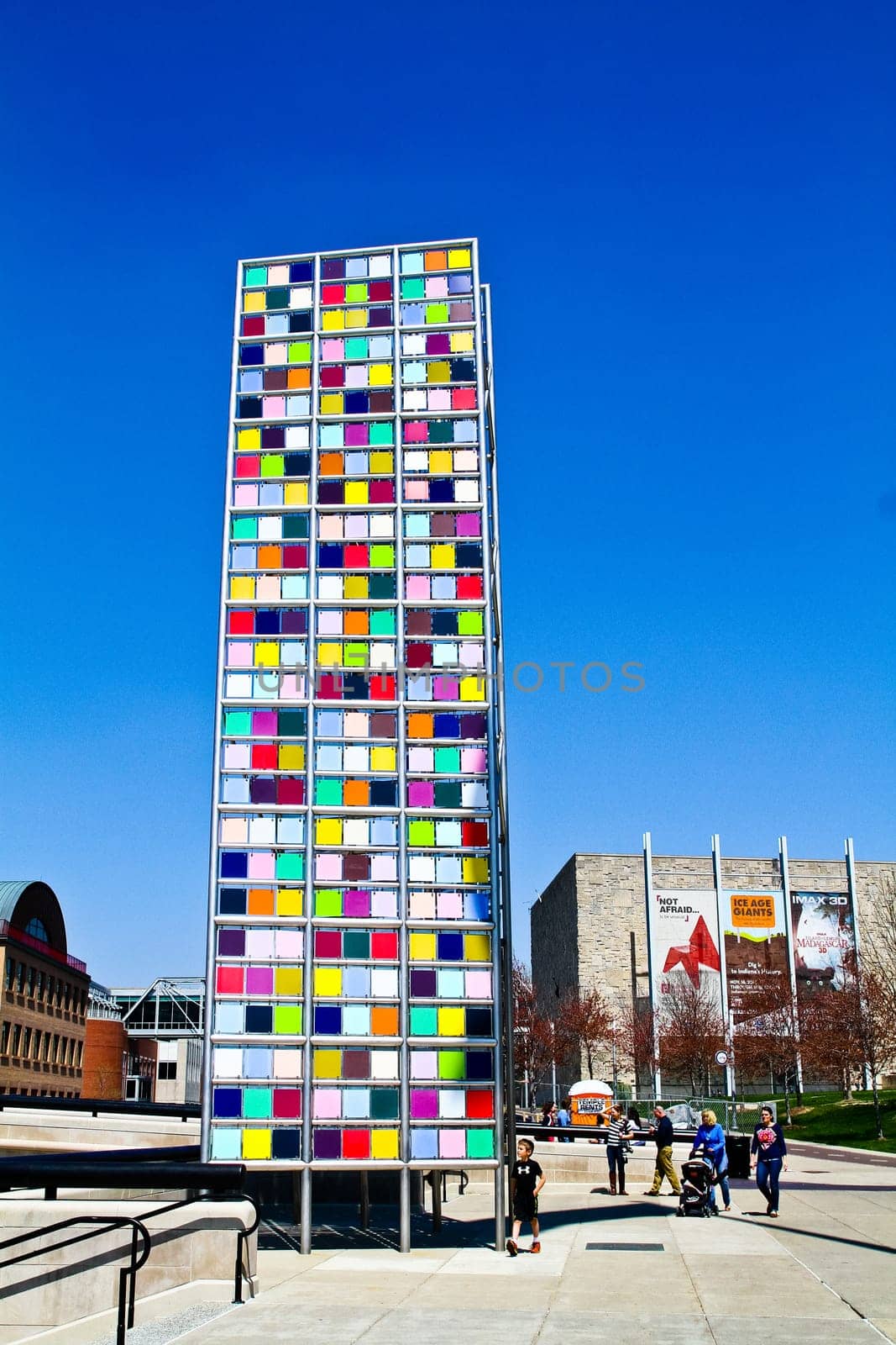 Vibrant urban sculpture in Indianapolis creates a modern, colorful focal point against a clear blue sky. The lively city atmosphere and diverse pedestrians add to the energetic and artistic appeal of this outdoor art installation.