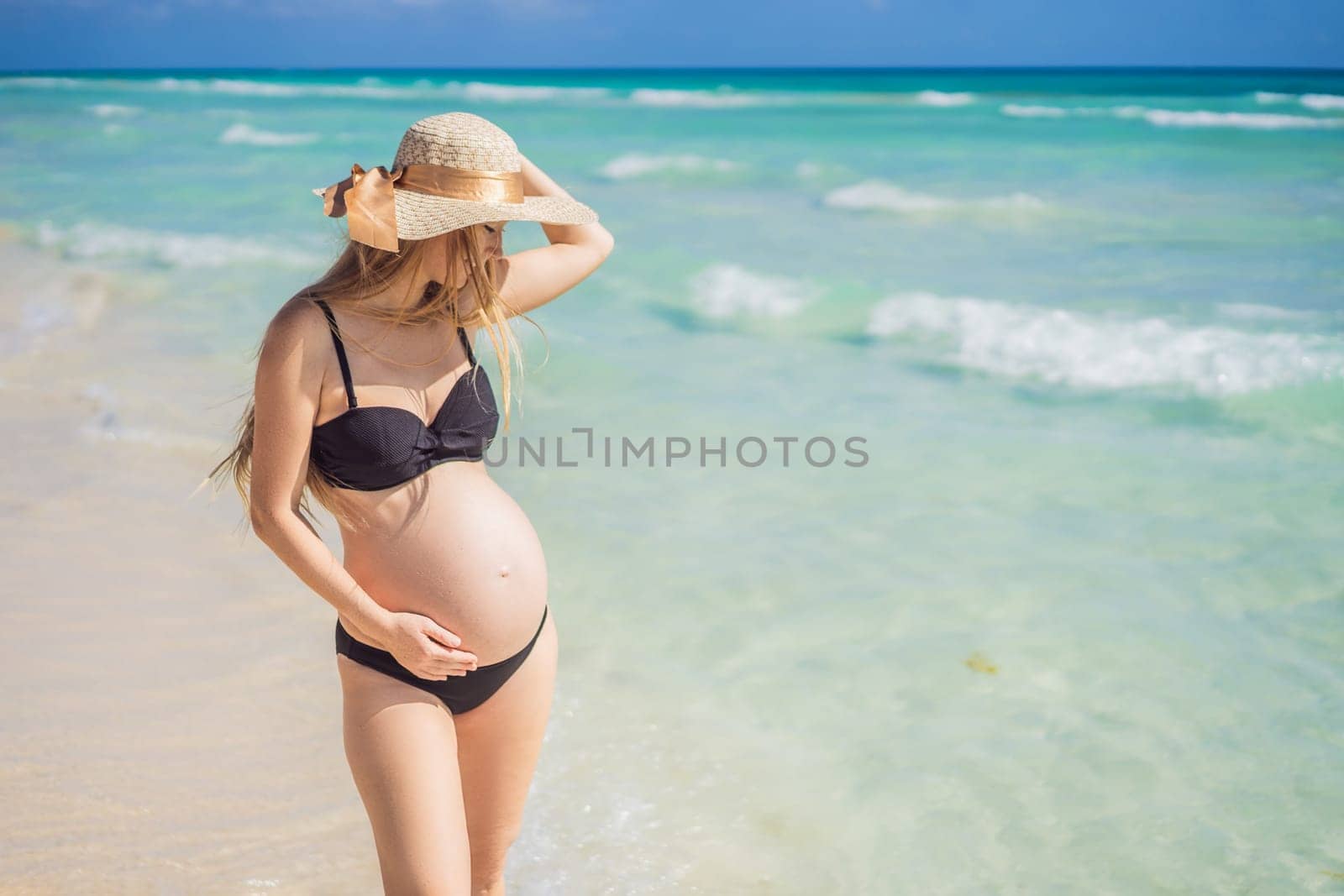 Radiant and expecting, a pregnant woman stands on a pristine snow-white tropical beach, celebrating the miracle of life against a backdrop of natural beauty.