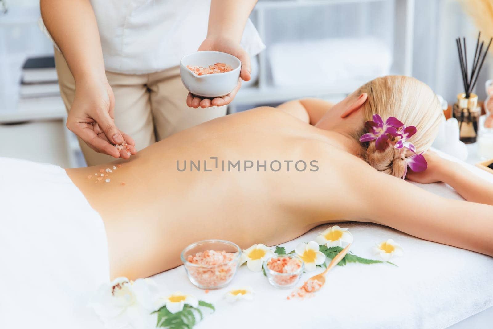 Woman customer having exfoliation treatment in luxury spa salon with warmth candle light ambient. Salt scrub beauty treatment in health spa body scrub. Quiescent