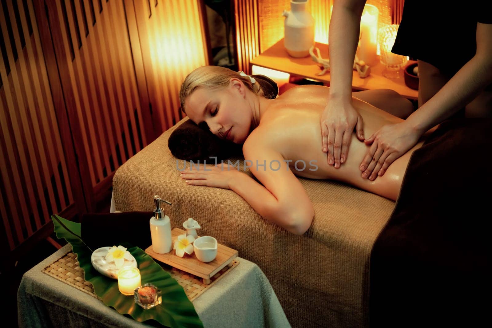 Caucasian woman customer enjoying relaxing anti-stress spa massage and pampering with beauty skin recreation leisure in warm candle lighting ambient salon spa at luxury resort or hotel. Quiescent