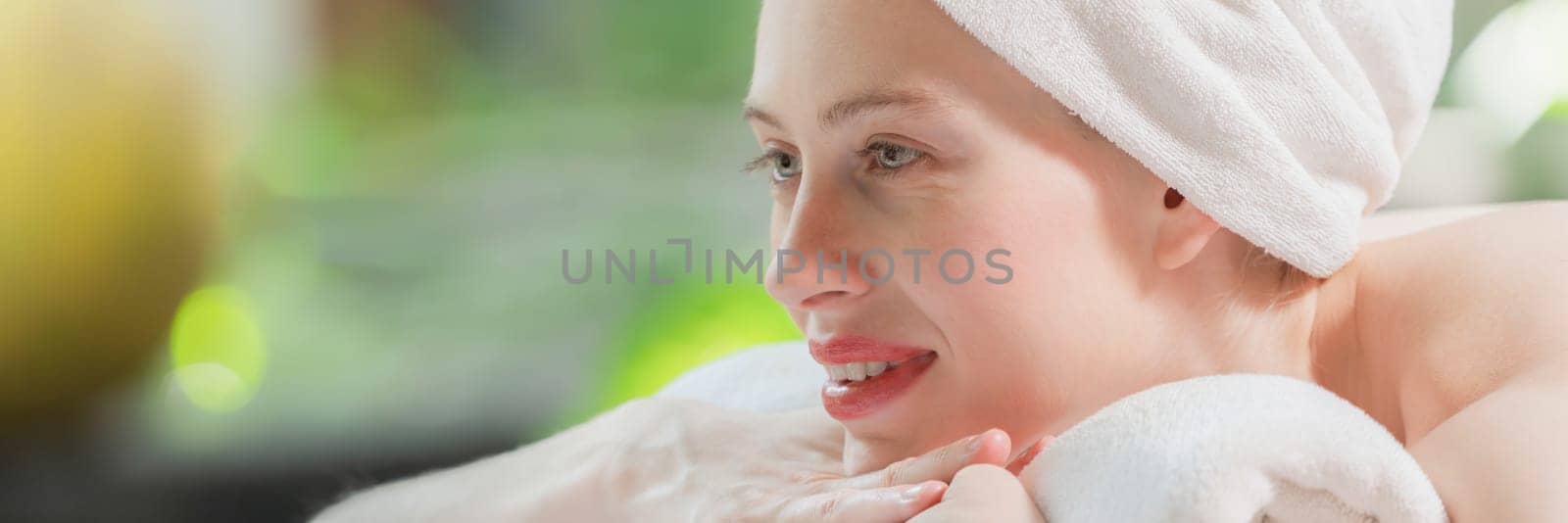 Closeup of beautiful women in white towel relaxes on spa bed surrounded by peaceful and calm nature. Young gorgeous female wearing white towel during waiting for body massage. Side view. Tranquility