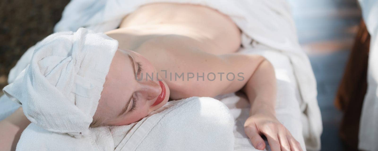 A top view portrait of a beautiful young caucasian woman with white towel rest on comfortable spa bed with relaxation. Close up of beautiful skin ready for having body massage. Tranquility.