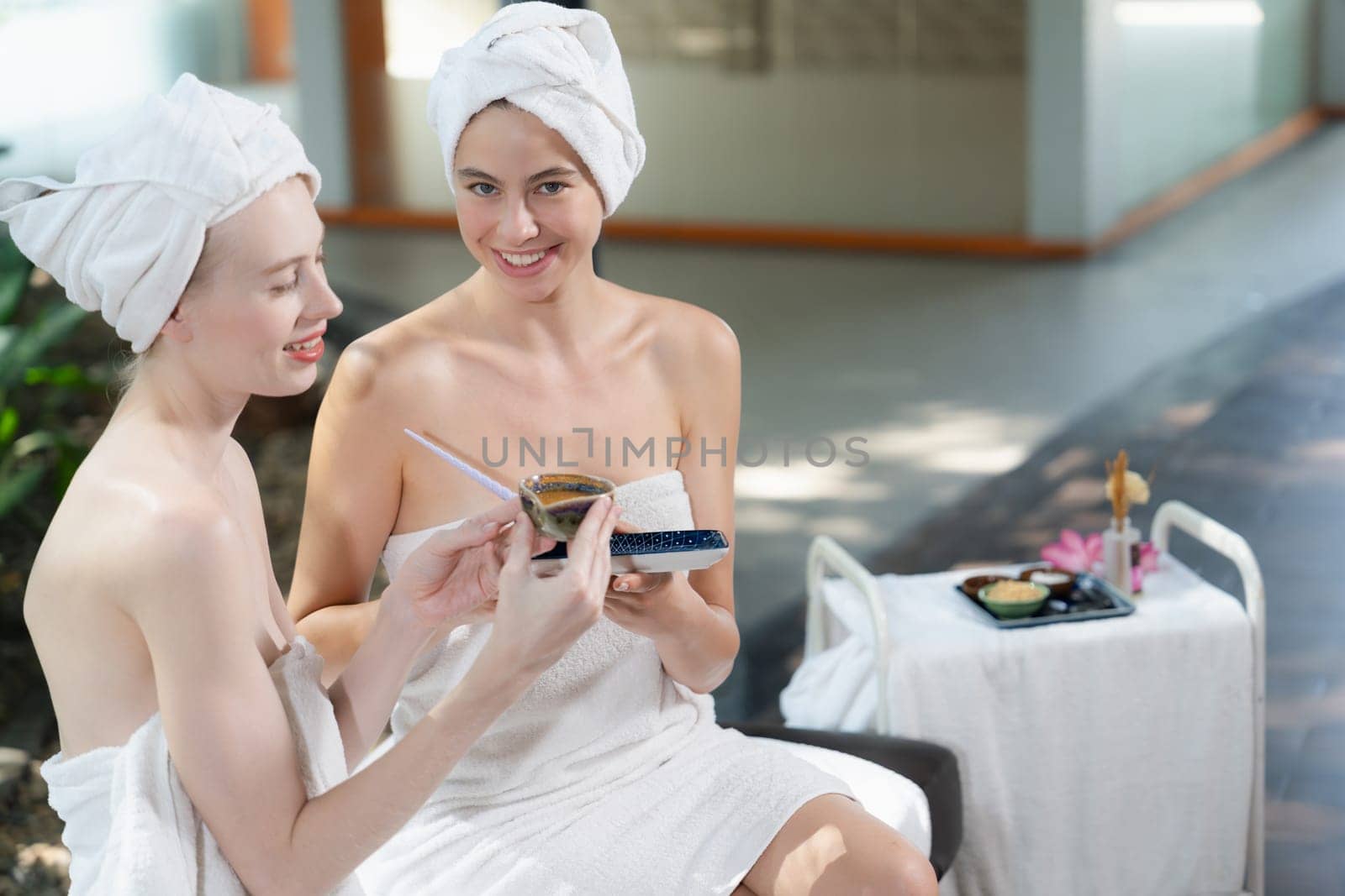 A portrait of two spa girls in white towel looking at camera while holding the homemade facial mask at outdoor surrounded by peaceful natural environment. Healthy and beauty concept. Tranquility.