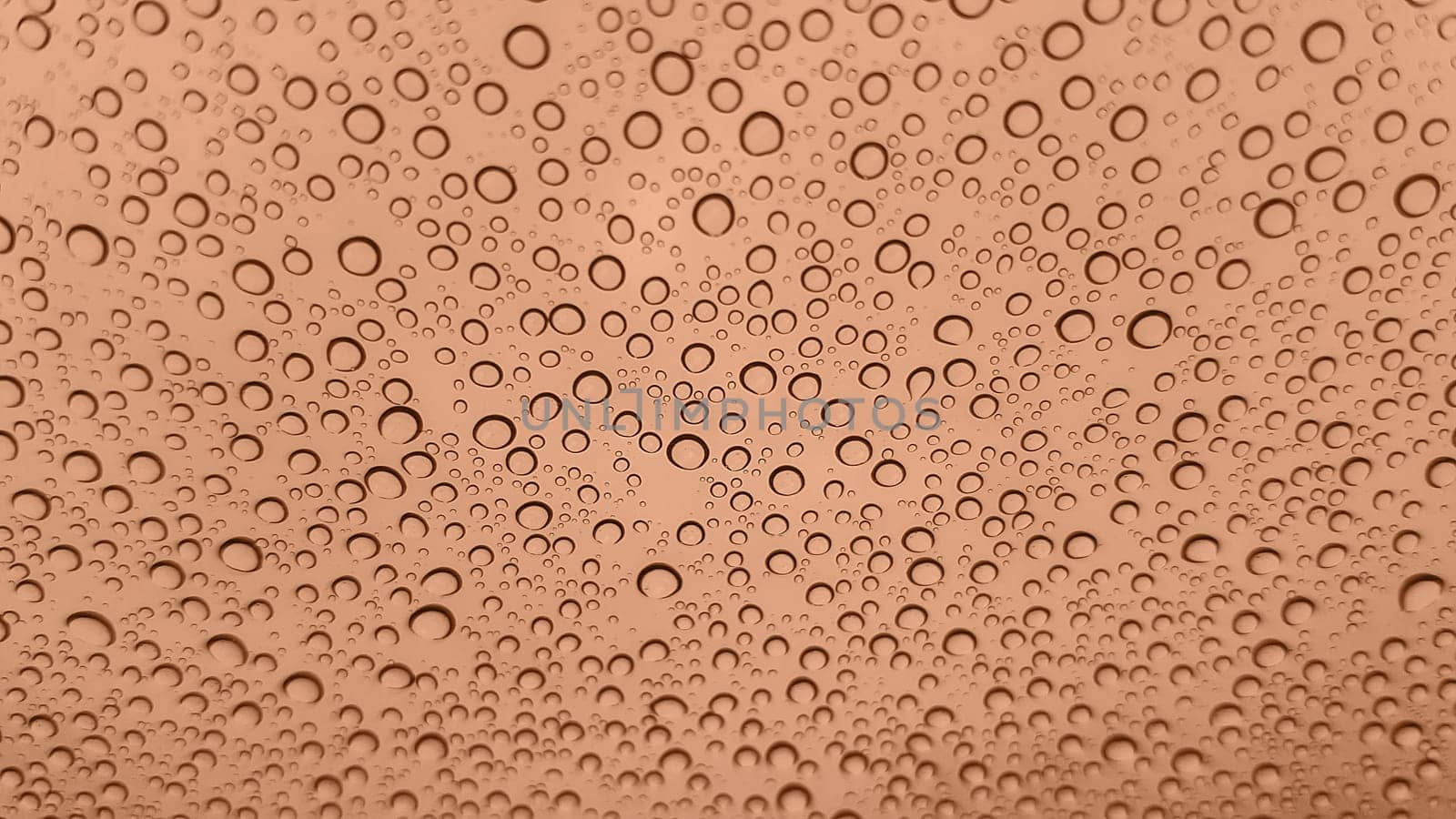 Abstract image of rain drops on glass. Image toned in Peach Fuzz color of the year 2024. New Fashion color. Top view. Abstract drops view