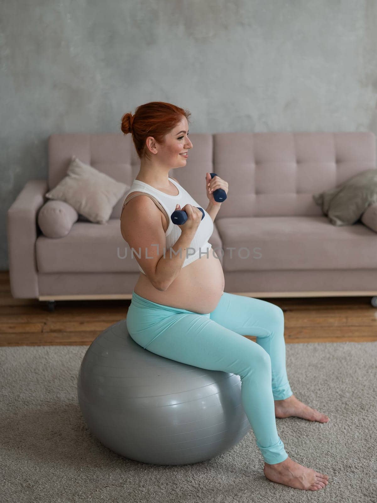 Pregnant woman doing exercises with dumbbells while sitting on a fitness ball at home