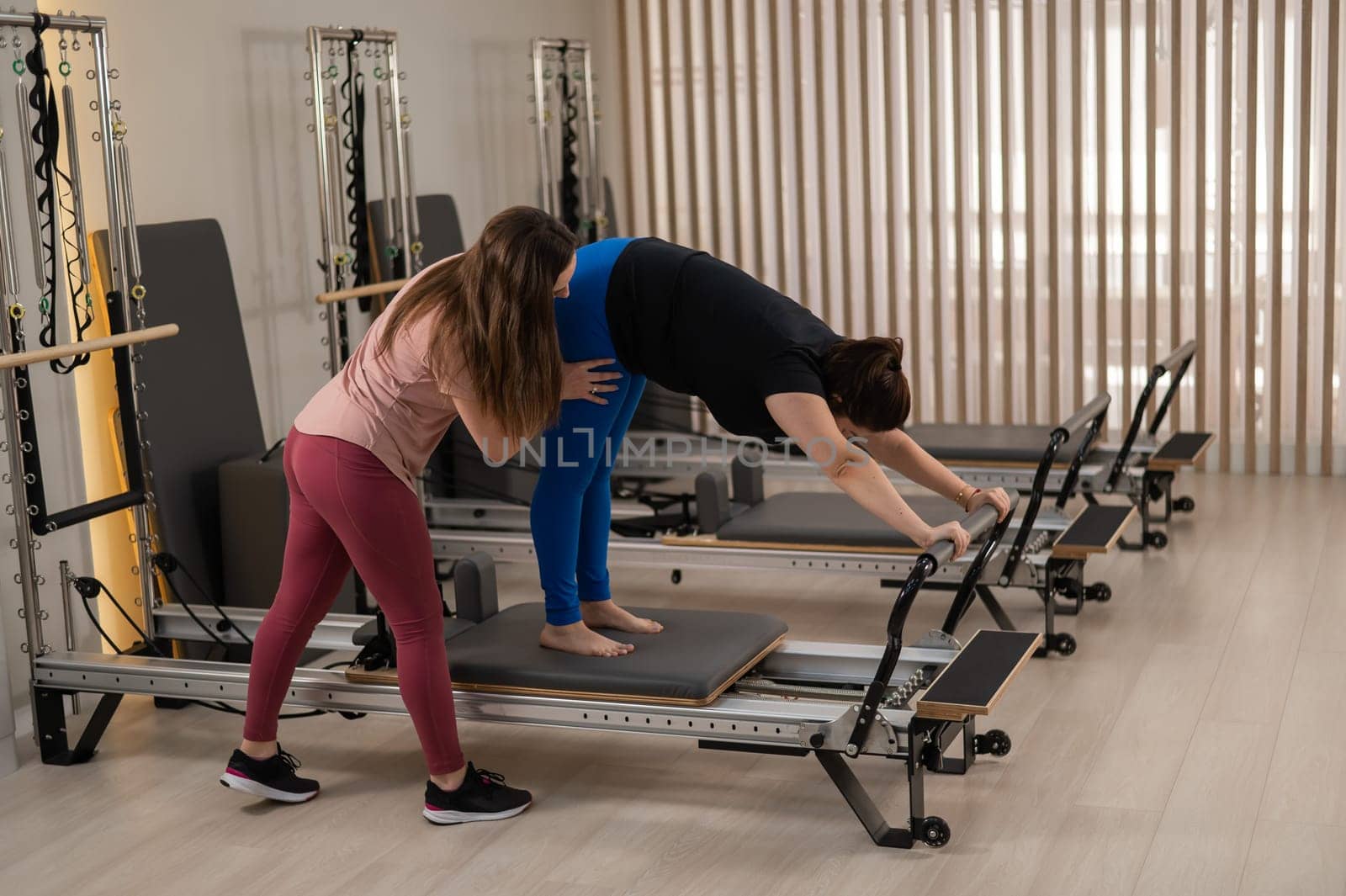 Overweight caucasian woman doing pilates exercises on reformer with personal trainer