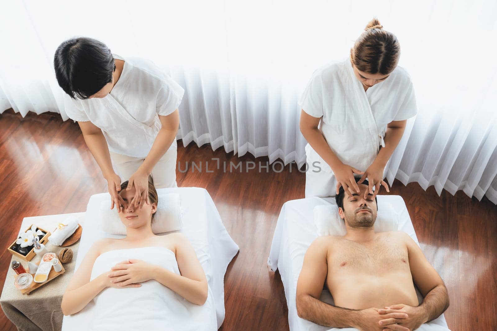 Caucasian couple enjoying relaxing anti-stress head massage and pampering facial beauty skin recreation leisure in dayspa modern light ambient at luxury resort or hotel spa salon. Quiescent