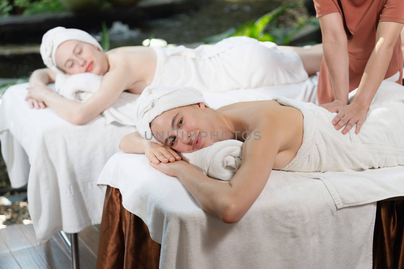 A portrait of two young attractive woman lie on bed during having back massage by a professional masseur at outdoor surrounded by peaceful natural environment. Healthy and beauty concept. Tranquility.
