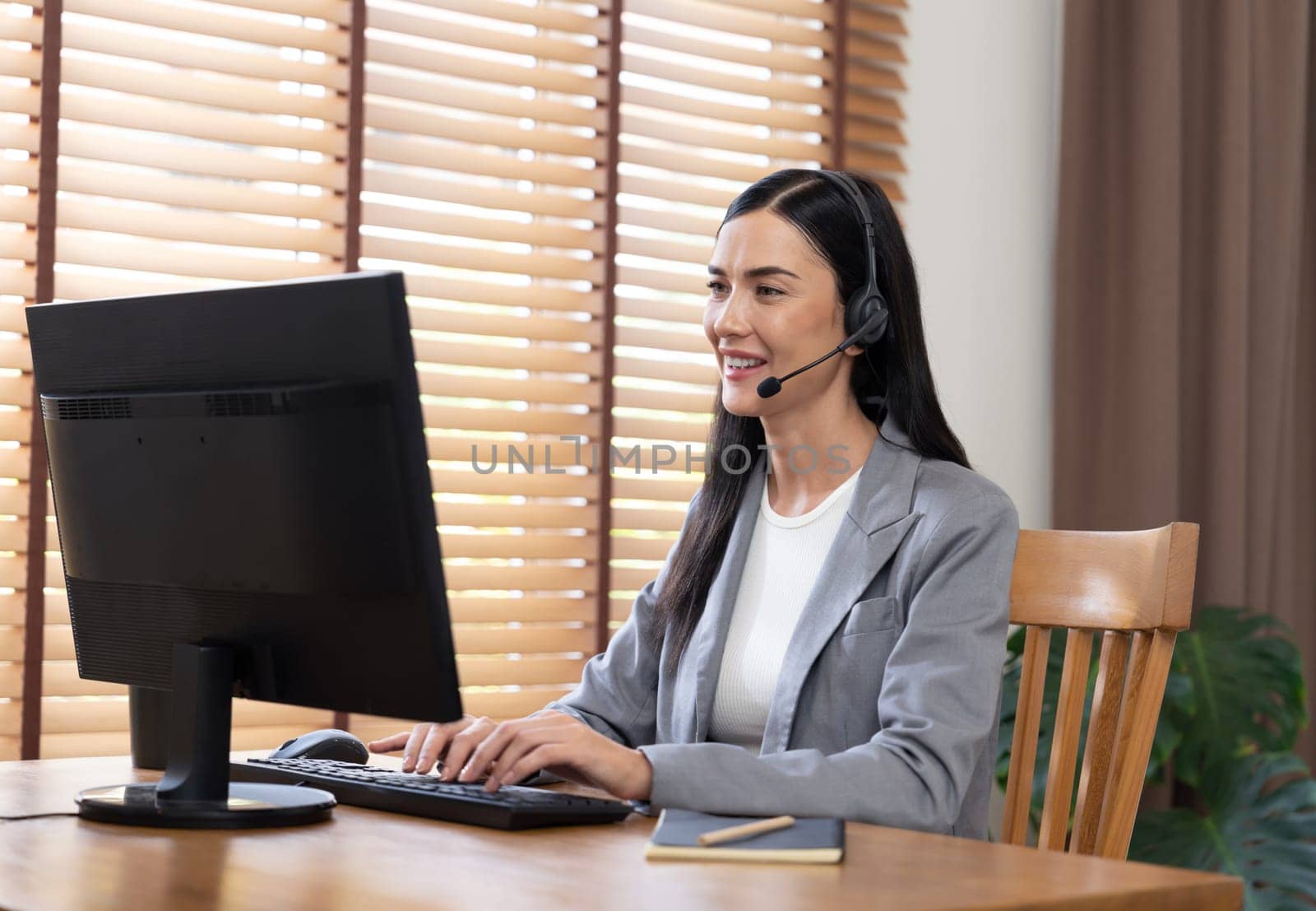 Female call center operator or customer service helpdesk staff working on workspace while talking on the headset to provide assistance for customer. Professional modern business service. Blithe