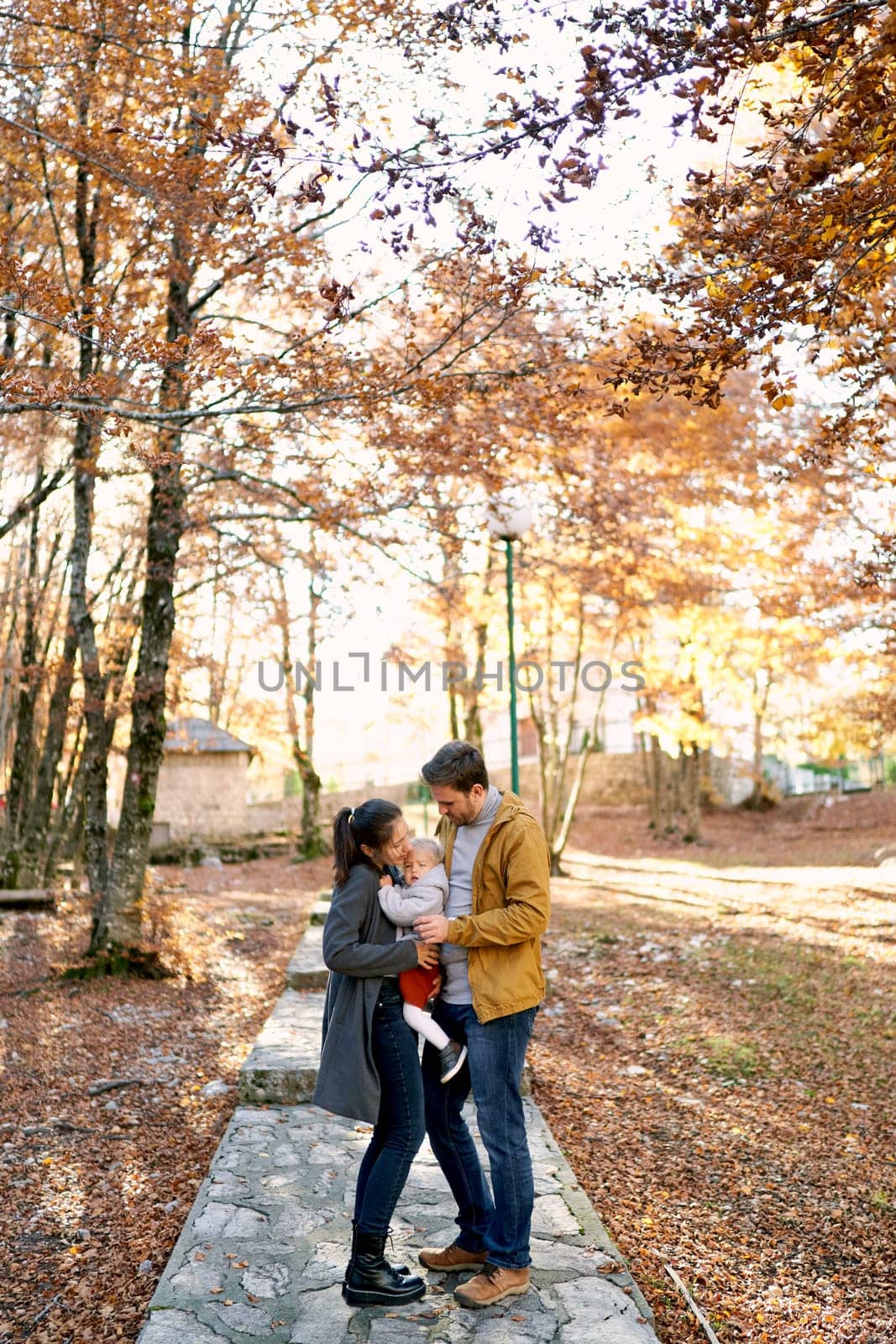 Dad stands next to mom correcting a little girl in her arms on a path in the forest. High quality photo