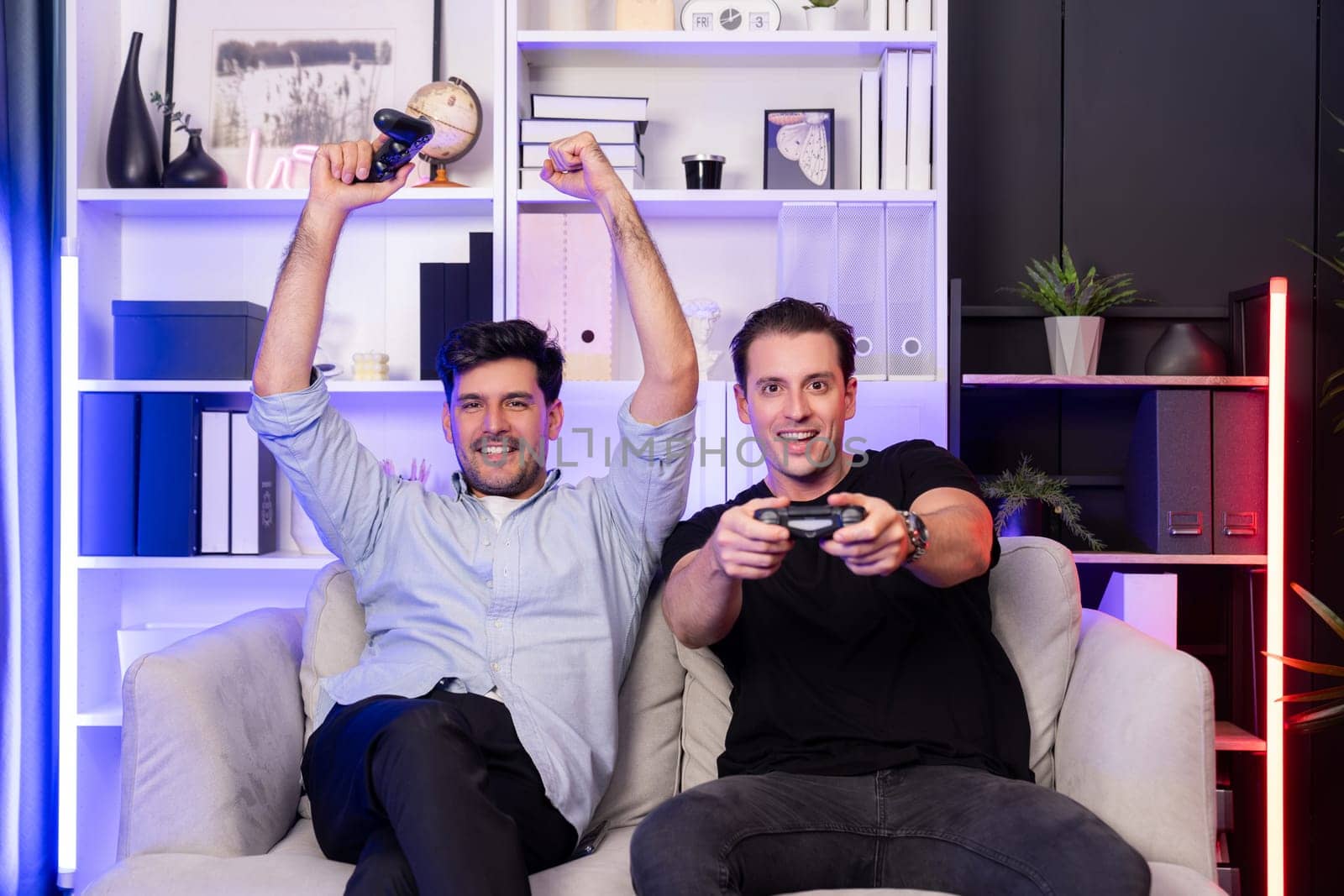 Winner and loser players of buddy friend gamers playing video game on TV using joysticks in studio room with neon blue light. Comfy living indoor at home place with cheerful fighting winner. Sellable.