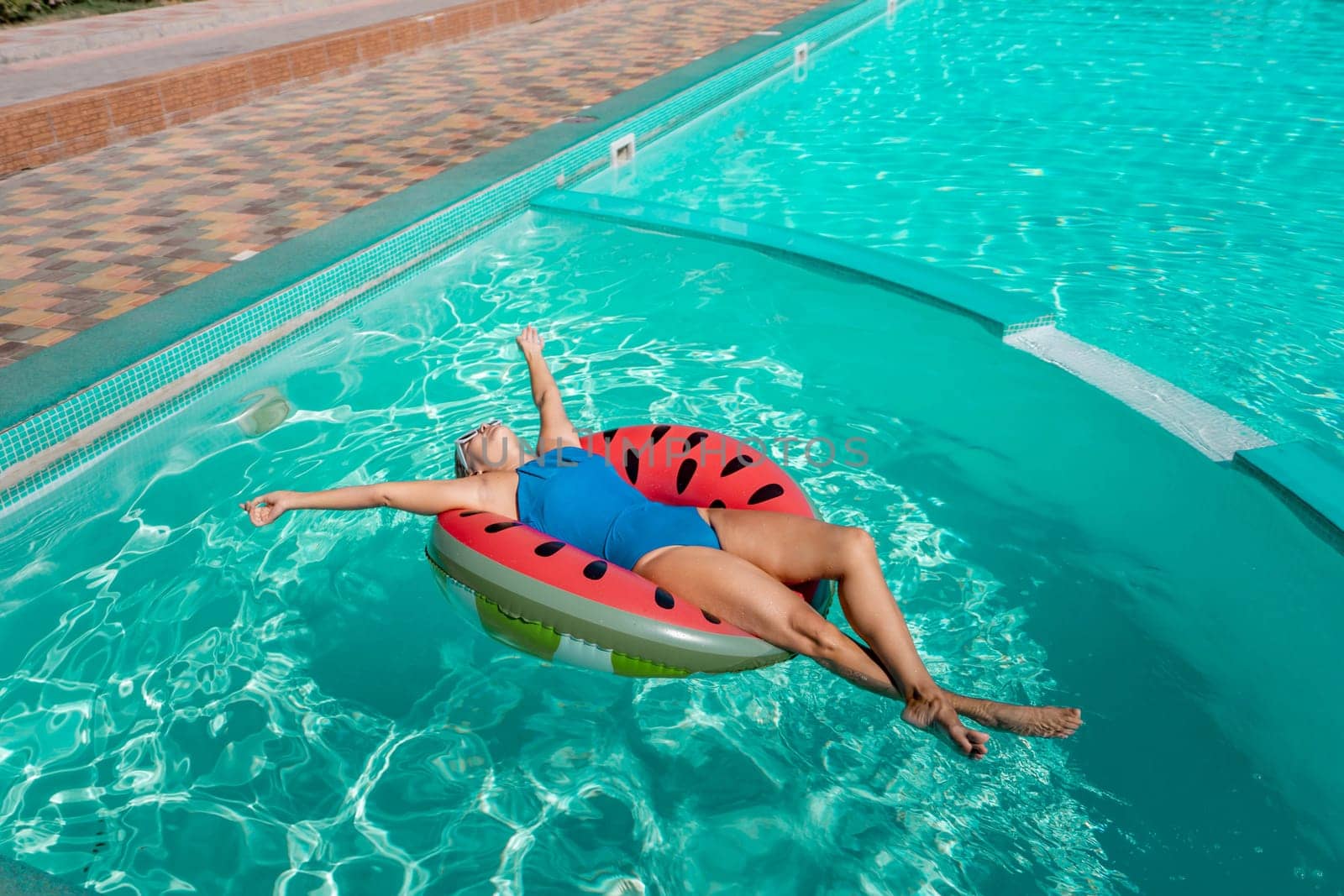 Happy woman in a swimsuit and sunglasses floating on an inflatable ring in the form of a watermelon, in the pool during summer holidays and vacations. Summer concept