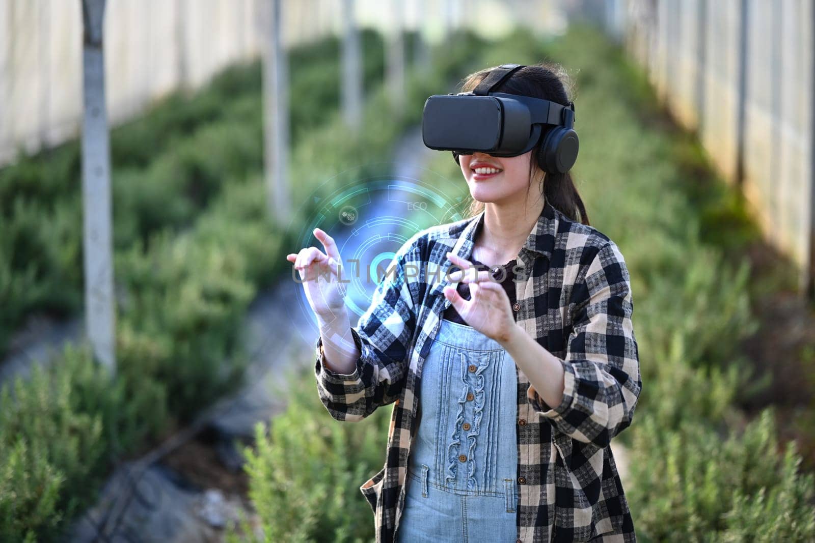 Female farmer wearing VR glasses standing in greenhouse. Innovative and smart farming concept