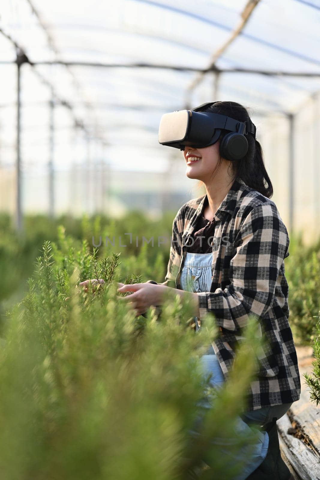 Female farmer wearing VR glasses standing in greenhouse. Innovative and smart farming concept