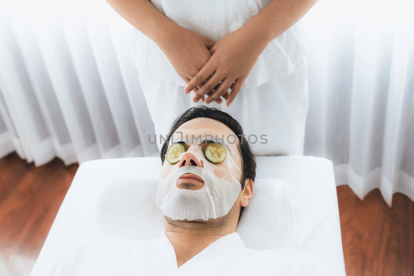 Serene daylight ambiance of spa salon, man customer indulges in rejuvenating with luxurious cucumber facial mask. Facial skincare treatment and beauty care concept. Quiescent