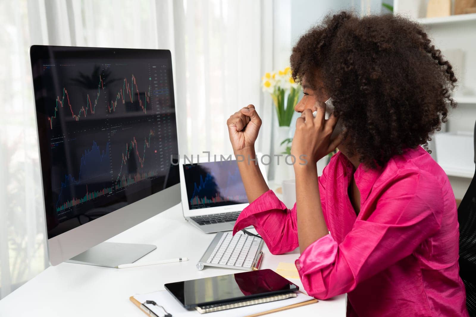 African woman blogger with serious face, looking on screen monitor and smartphone with stock market achievement at high profit. Concept of exchange investment online in trading on pc. Tastemaker.