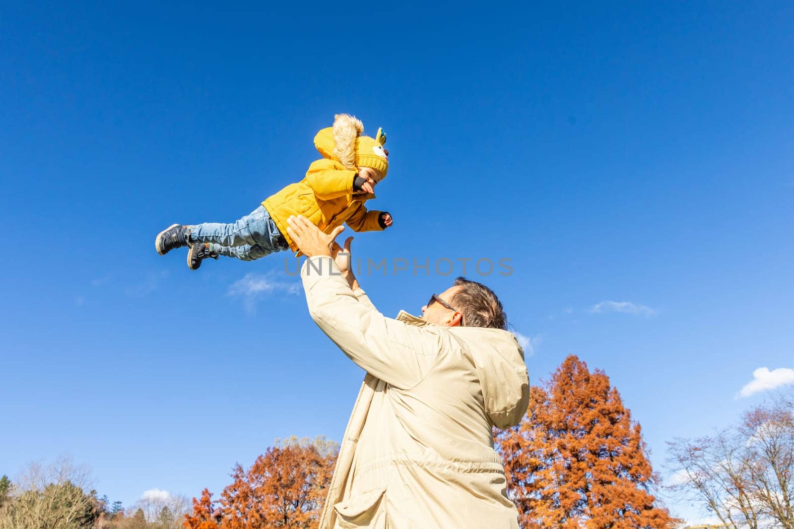 More, more,... dad, that's fun. Happy young father throws his cute little baby boy up in the air. Father's Day, Father and his son baby boy playing and hugging outdoors in nature in fall