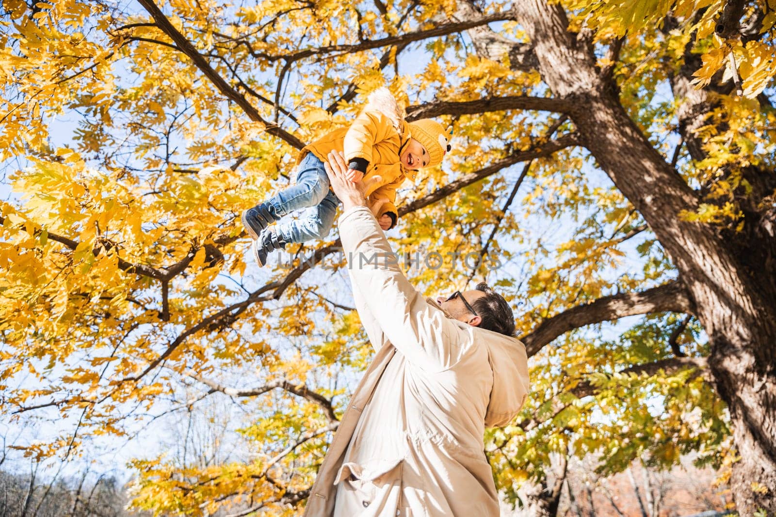 More, more,...dad, that's fun. Happy young father throws his cute little happy baby boy up in the air. Father's Day, Father and his son baby boy playing and hugging outdoors in nature in fall. by kasto