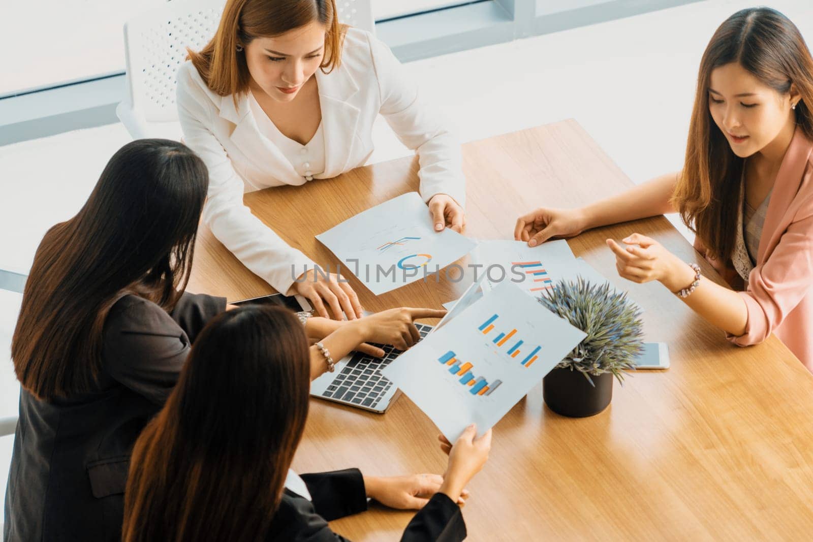 Businesswoman in group meeting discussion with other businesswomen colleagues in modern workplace office with laptop computer and documents on table. People corporate business work team concept. uds