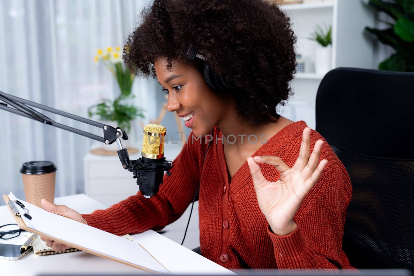 Host channel of beautiful African woman influencer talking with listeners in broadcast studio with script note. Time slot of life coach consultant on live social media online. Tastemaker.