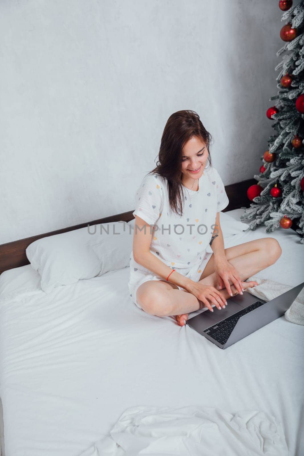 Woman working online on laptop in bedroom on bed new year by Simakov
