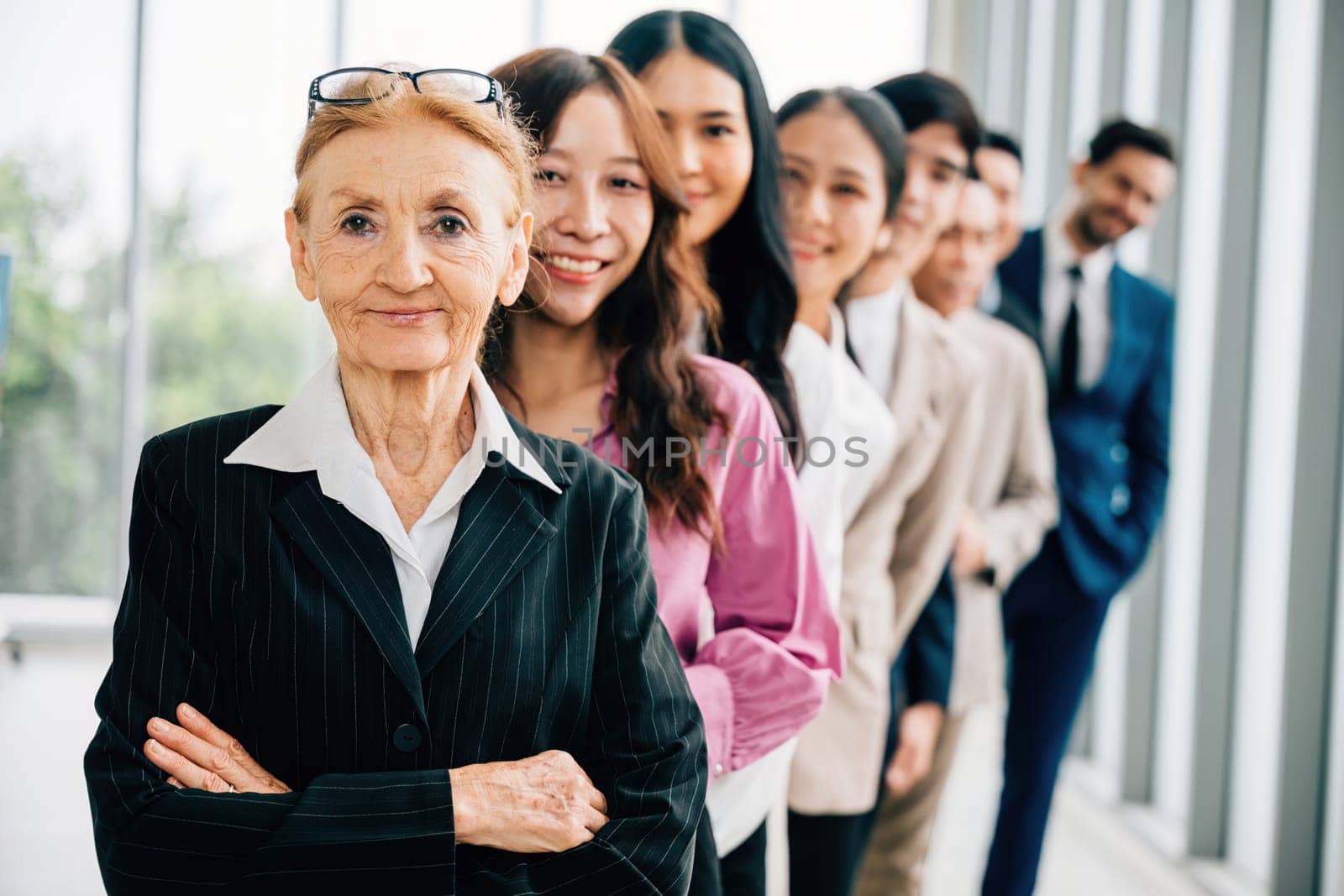 Young businesspeople and senior woman confidently looking camera in the office symbolize thriving business team with crossed arms. Their unity and commitment to success shine through in their startup.