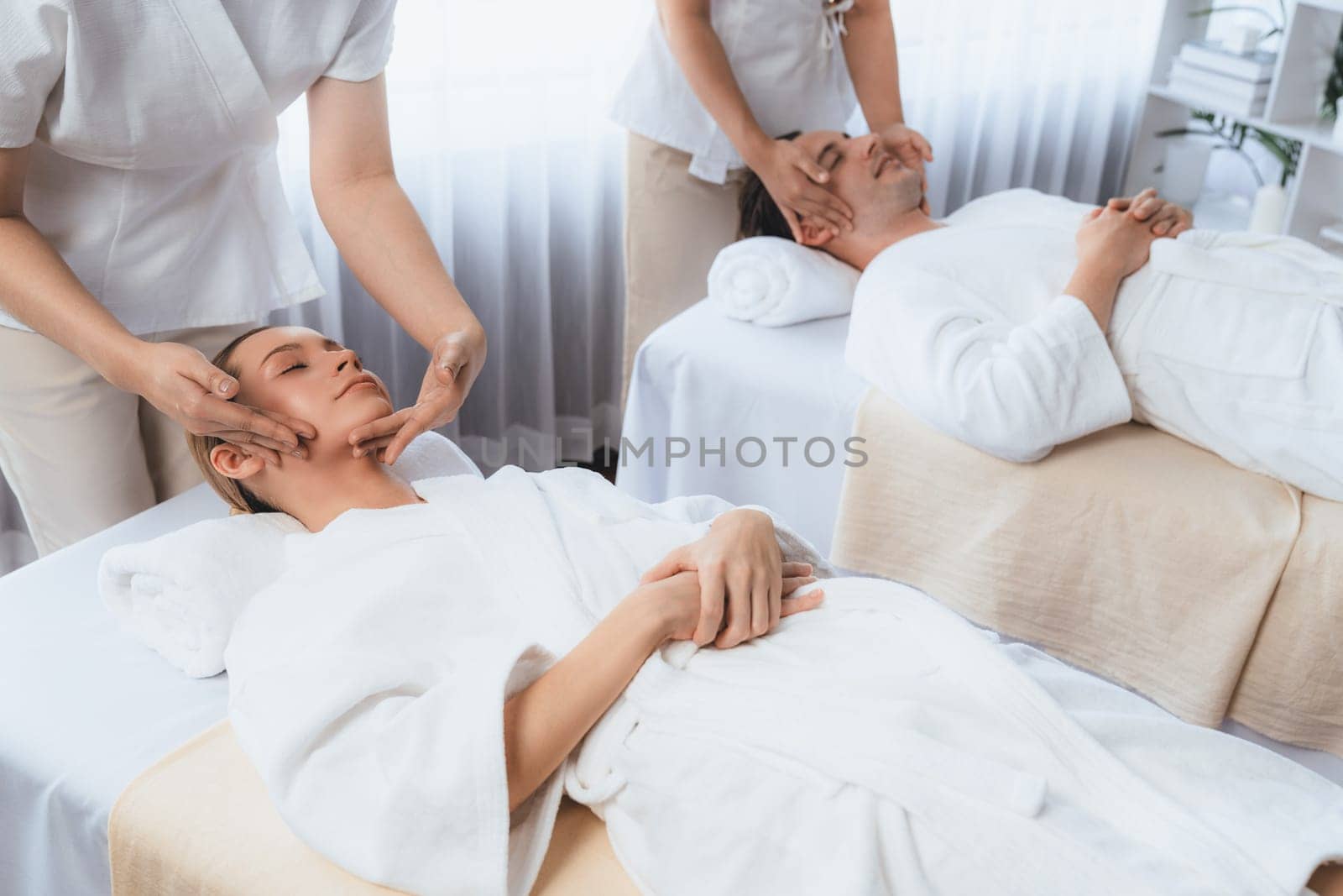 Caucasian couple enjoying relaxing anti-stress head massage and pampering facial beauty skin recreation leisure in dayspa modern light ambient at luxury resort or hotel spa salon. Quiescent