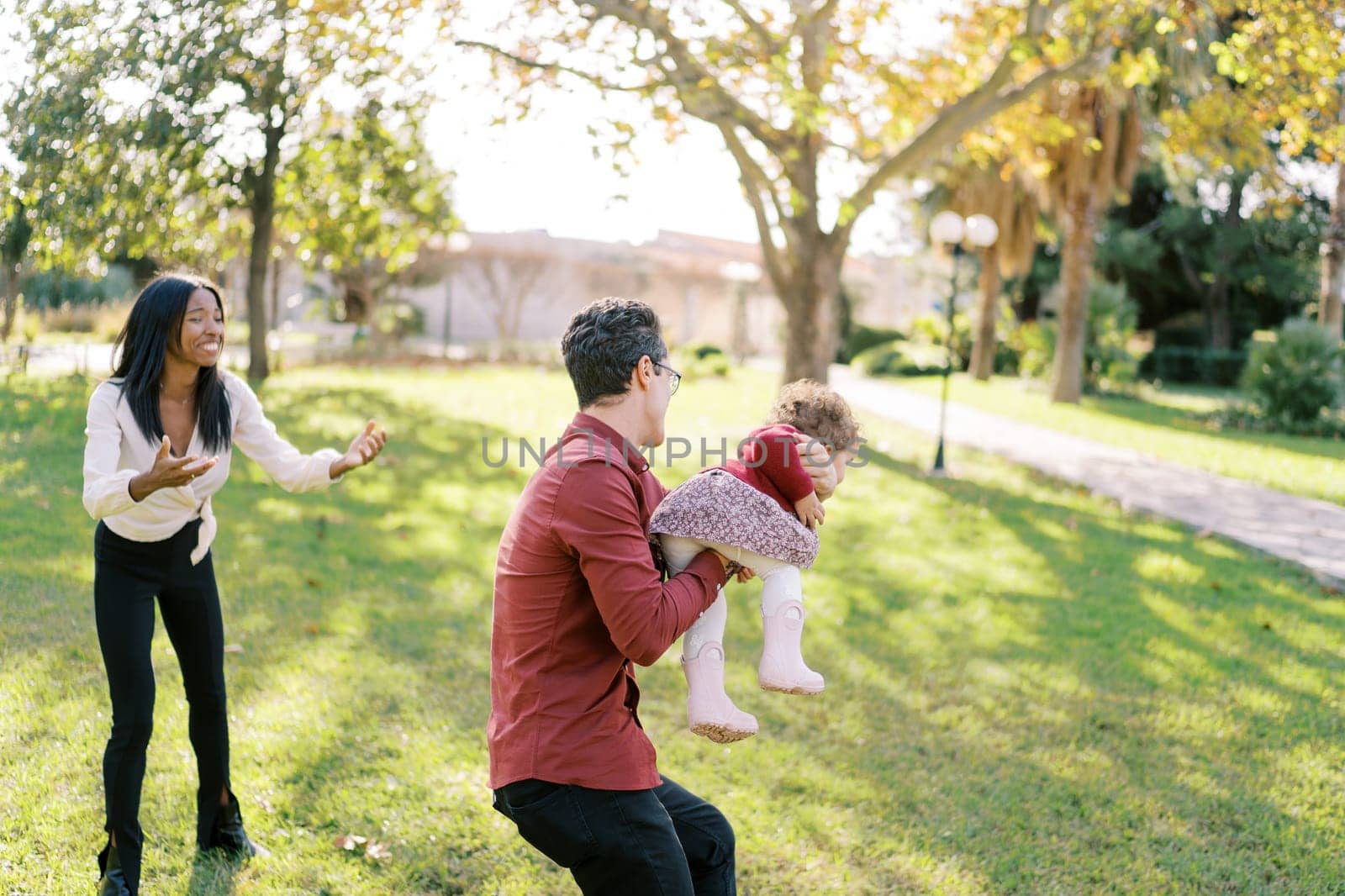 Laughing mom stretches her hands to the little girl who is circling dad in the park. High quality photo