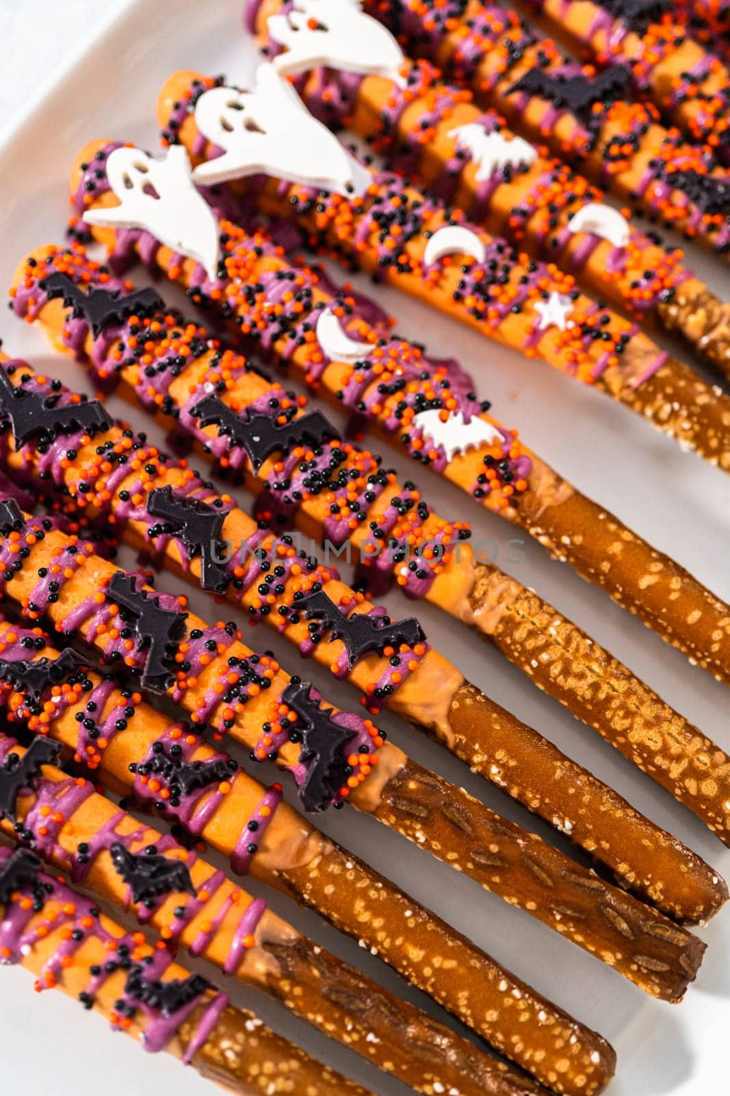 Halloween chocolate-covered pretzel rods with sprinkles on a white serving plate.