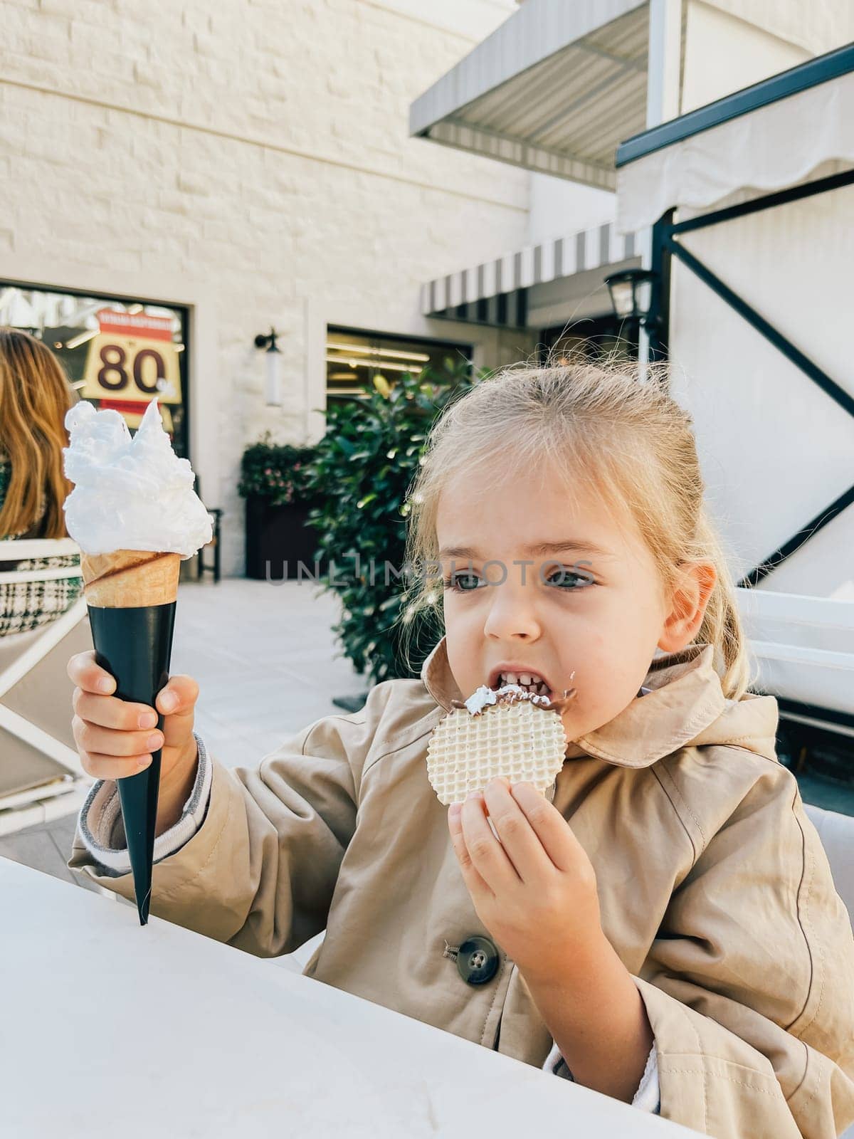 Little girl eats a waffle from an ice cream cone while sitting at the table. High quality photo