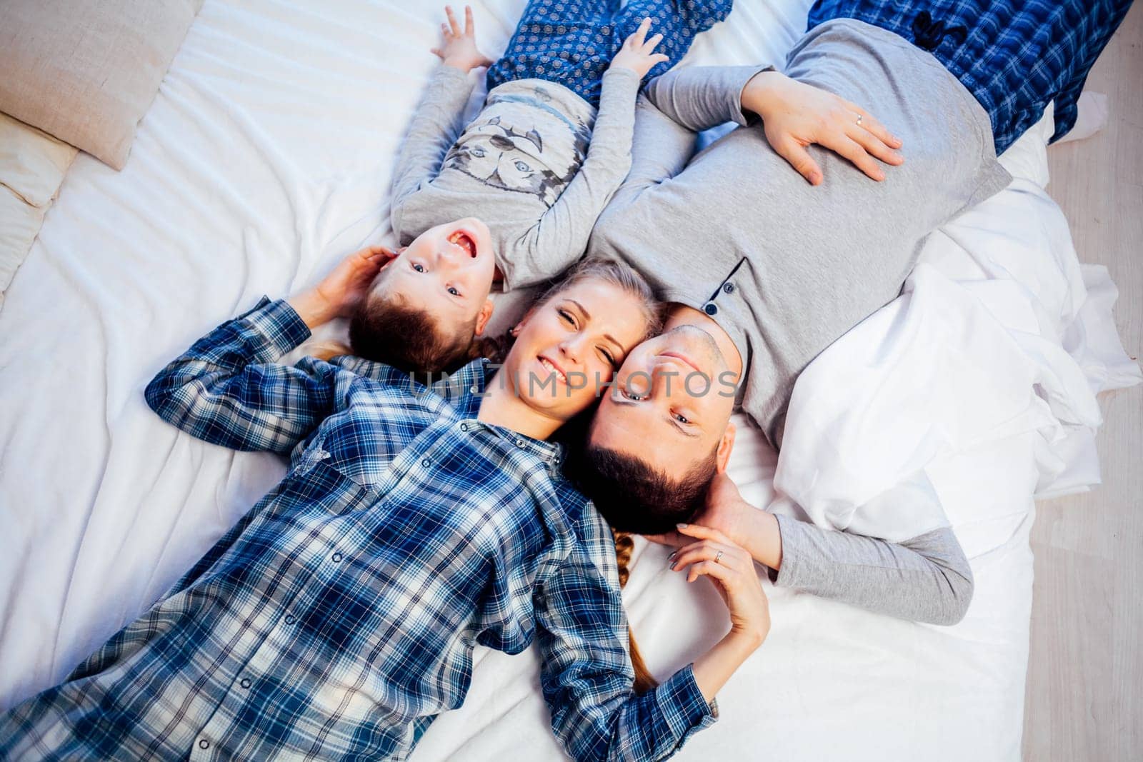 mom dad and son in the morning lying on the bed at home by Simakov