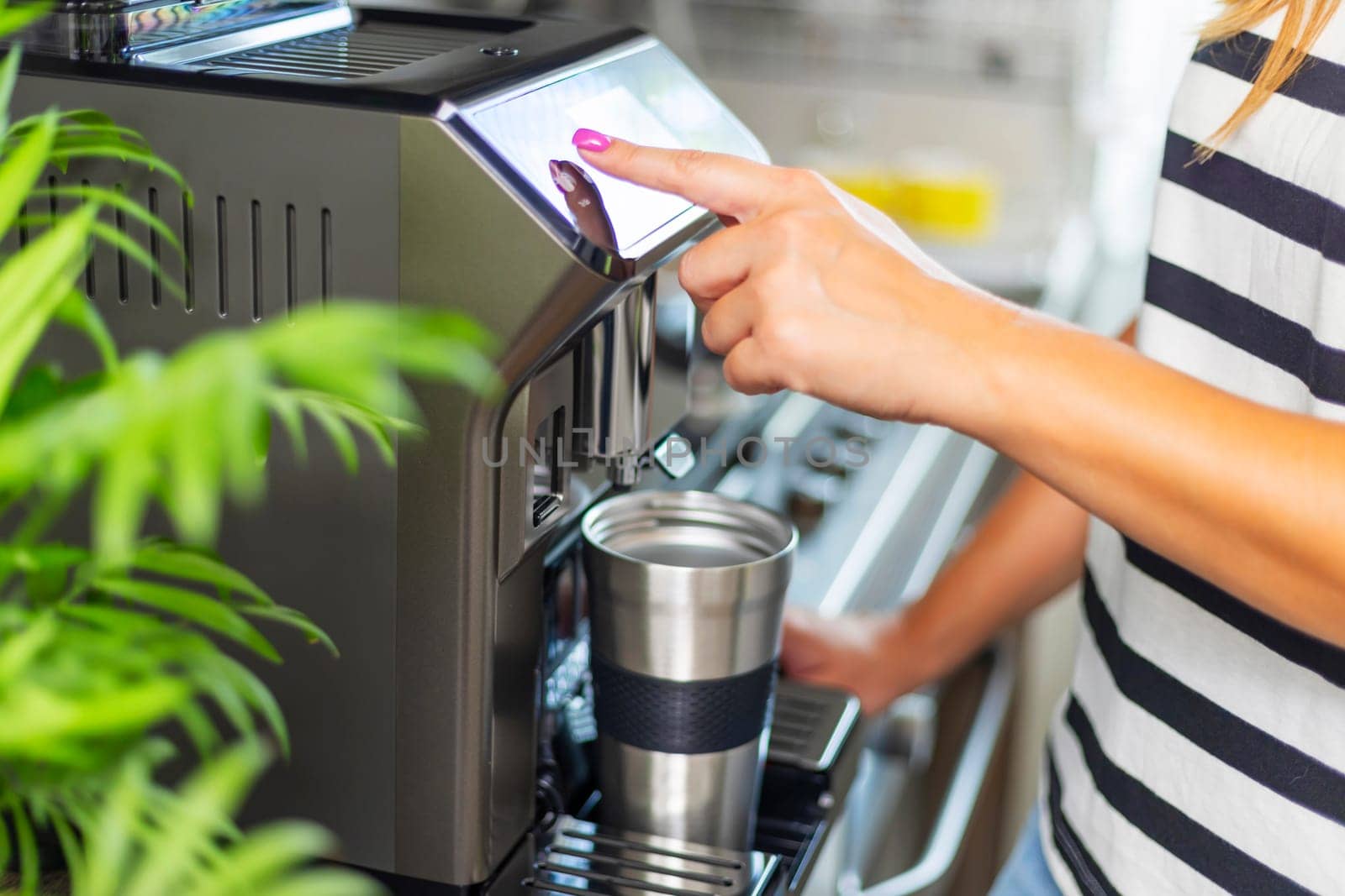 A young woman makes fresh flavored coffee with a modern coffee machine in her kitchen.