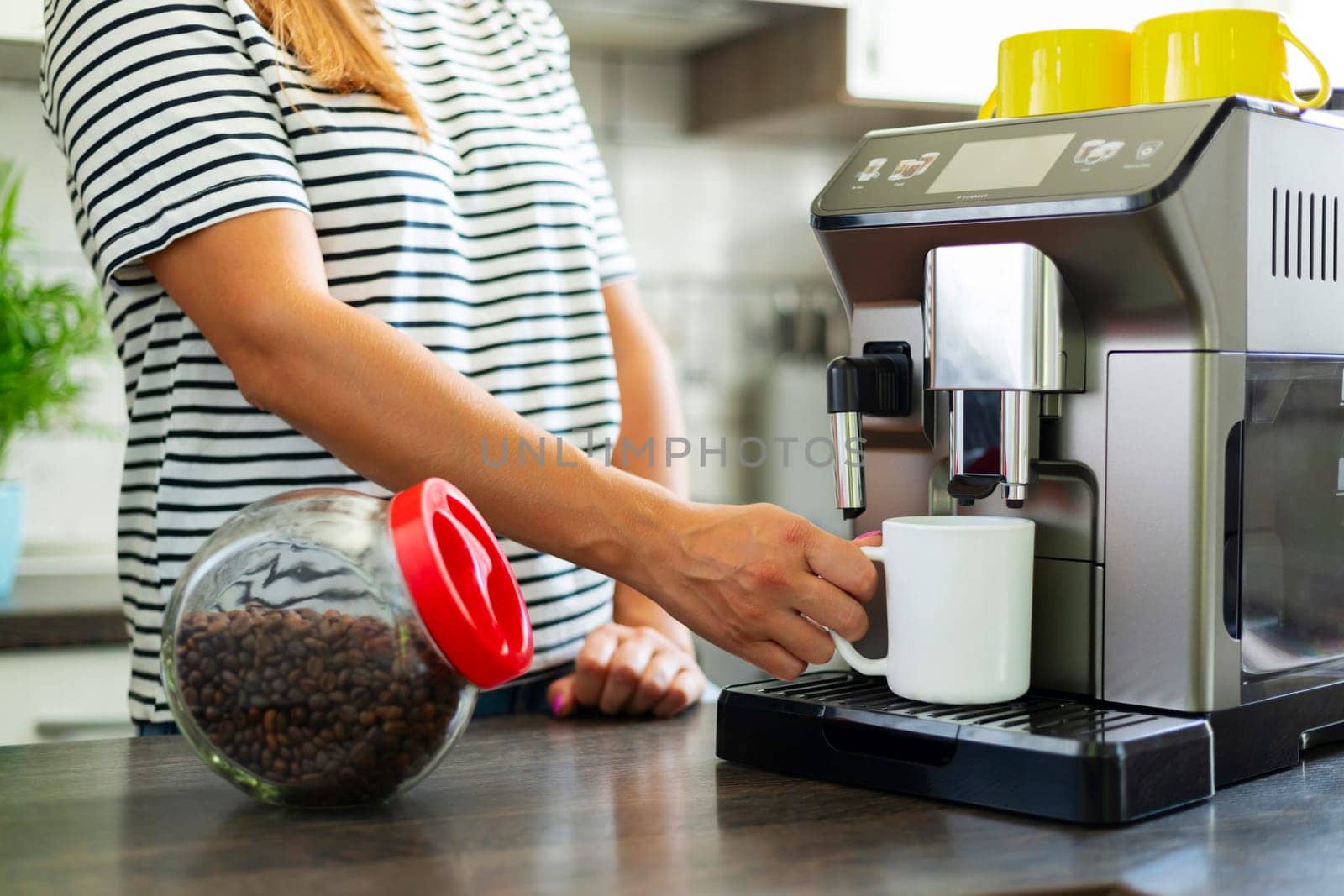 A young woman makes fresh flavored coffee with a modern coffee machine in her kitchen.