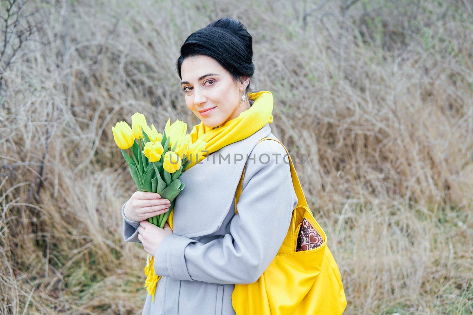 Portrait of brunette in coats with yellow tulips on the street